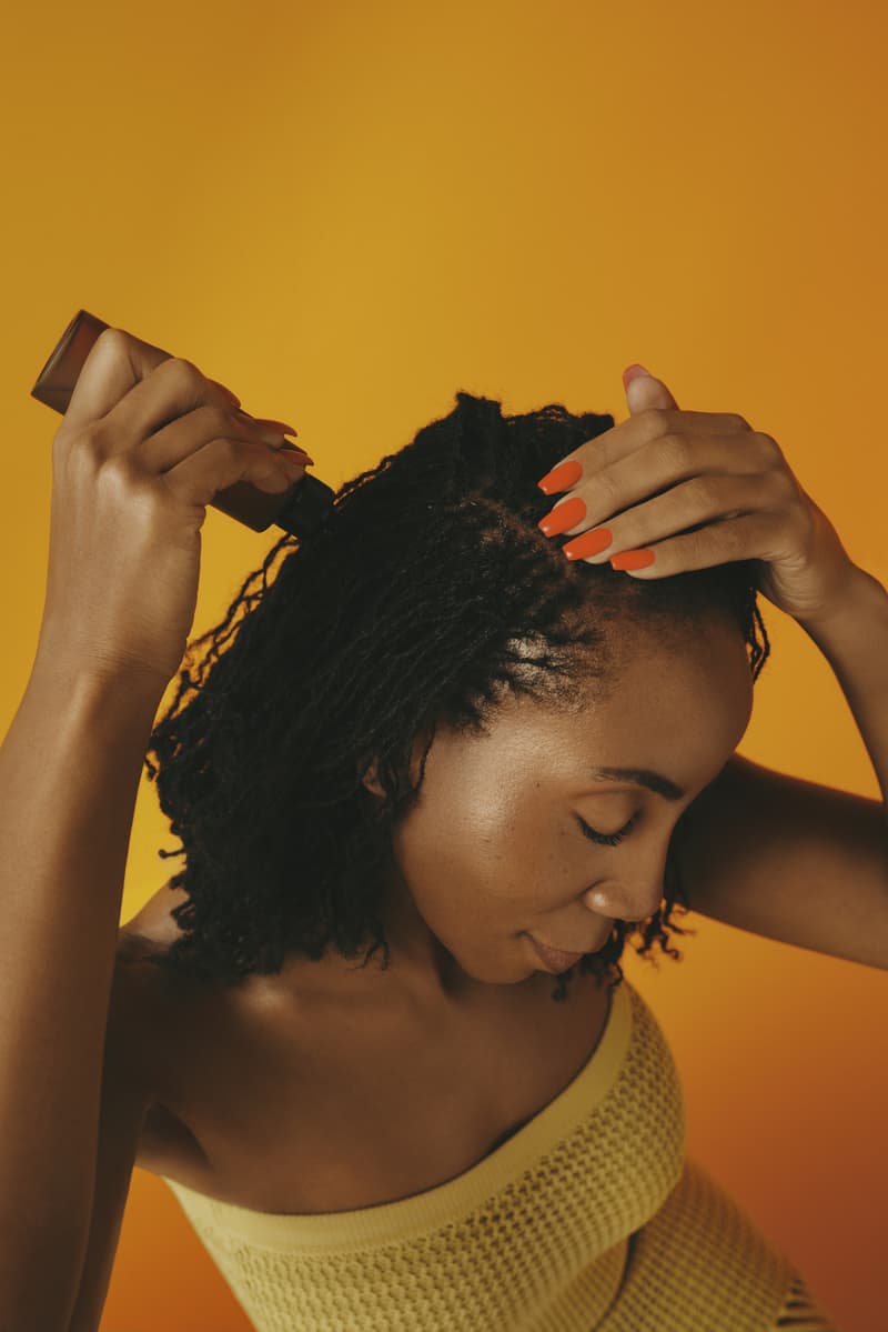 woman with bantu knots poses with pattern beauty haircare products, hair steamer, tracee ellis ross