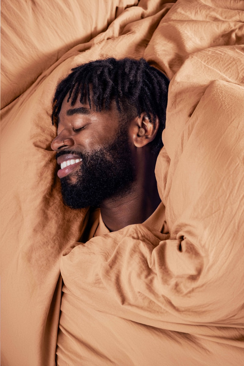 person sleeping inside of grey blankets with loops sleep ear plugs on, beauty