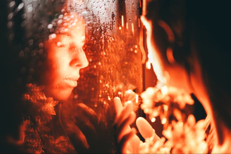 woman looking at her reflection with sakura flowers in red light, pheromone perfume, do they actually work