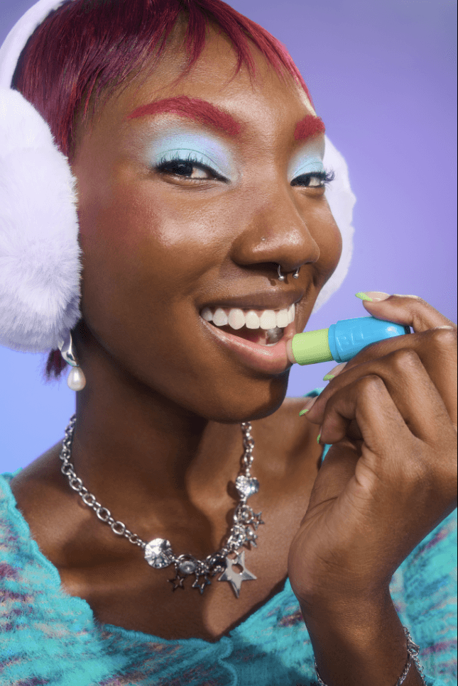 woman with bright blue eyeshadow and ear muffs applying bubble skincare new mint lip balm, beauty, gen-z