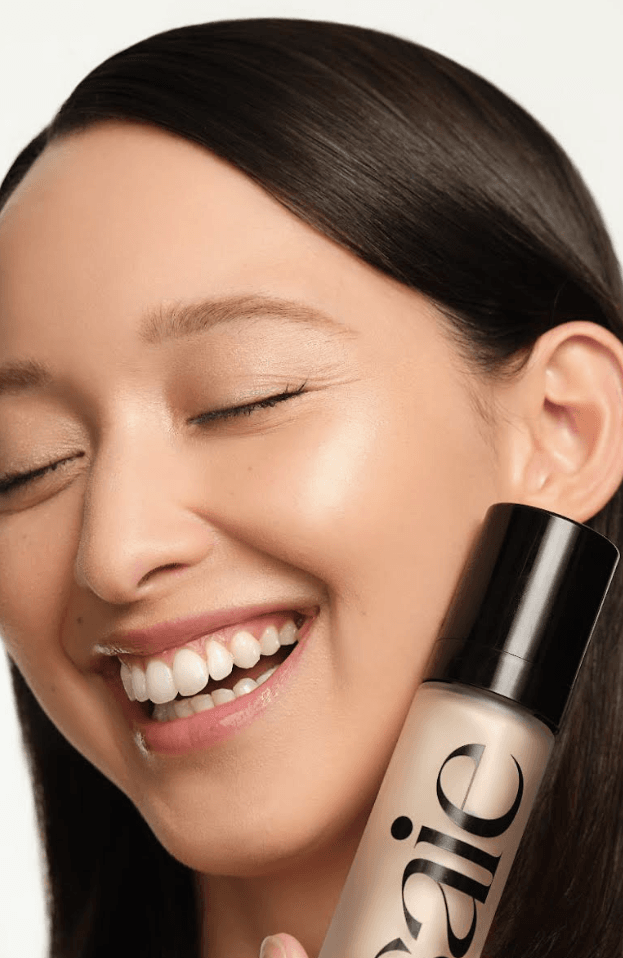 woman caressing bottle of saie beauty glowy super gel in warm glow, swatch of highlighting primer, makeup, skincare