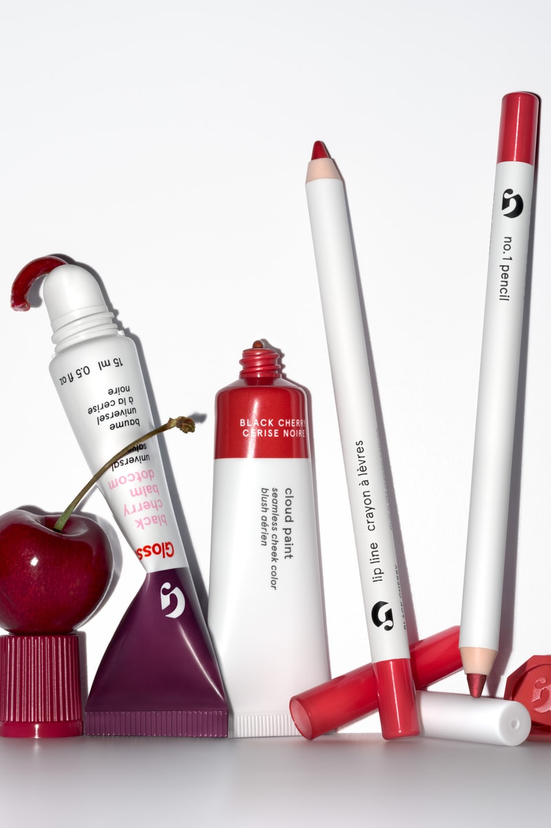 woman posing on top of a convertible with glossier balm dot com in her hand, black cherry collection, makeup, skincare