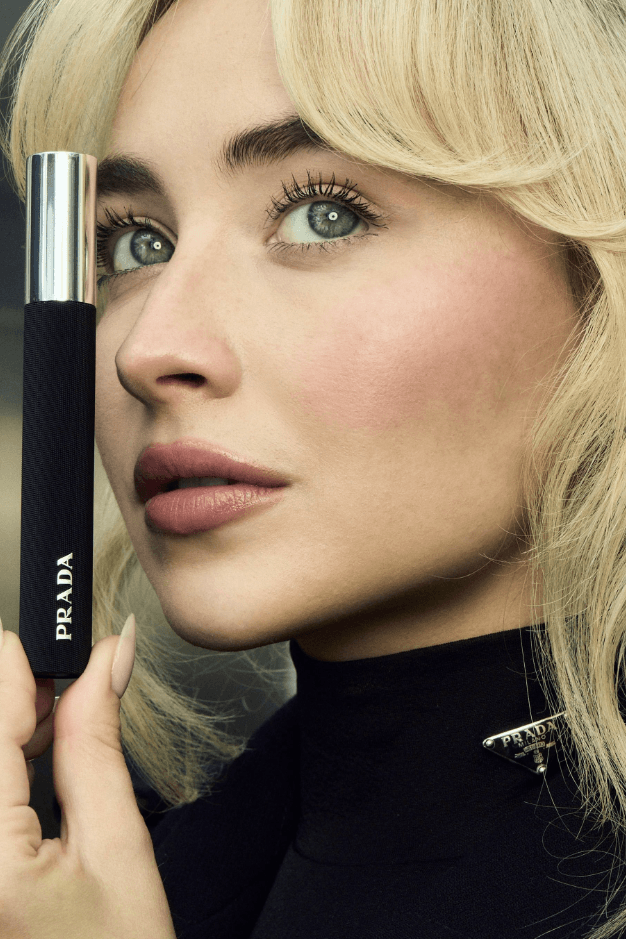 sabrina carpenter holding prada mascara with big bouncy hair, makeup, beauty