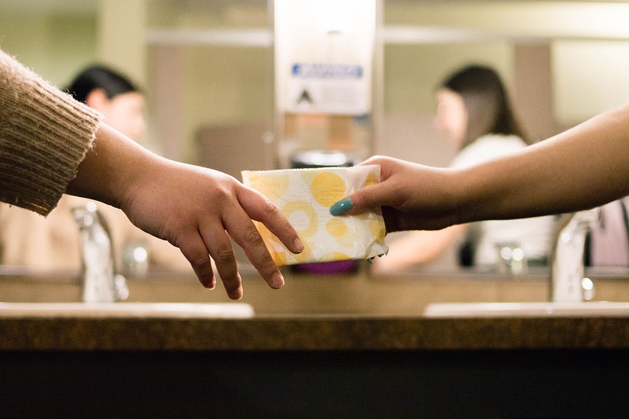 Woman handing sanitary pad to another woman in restroom