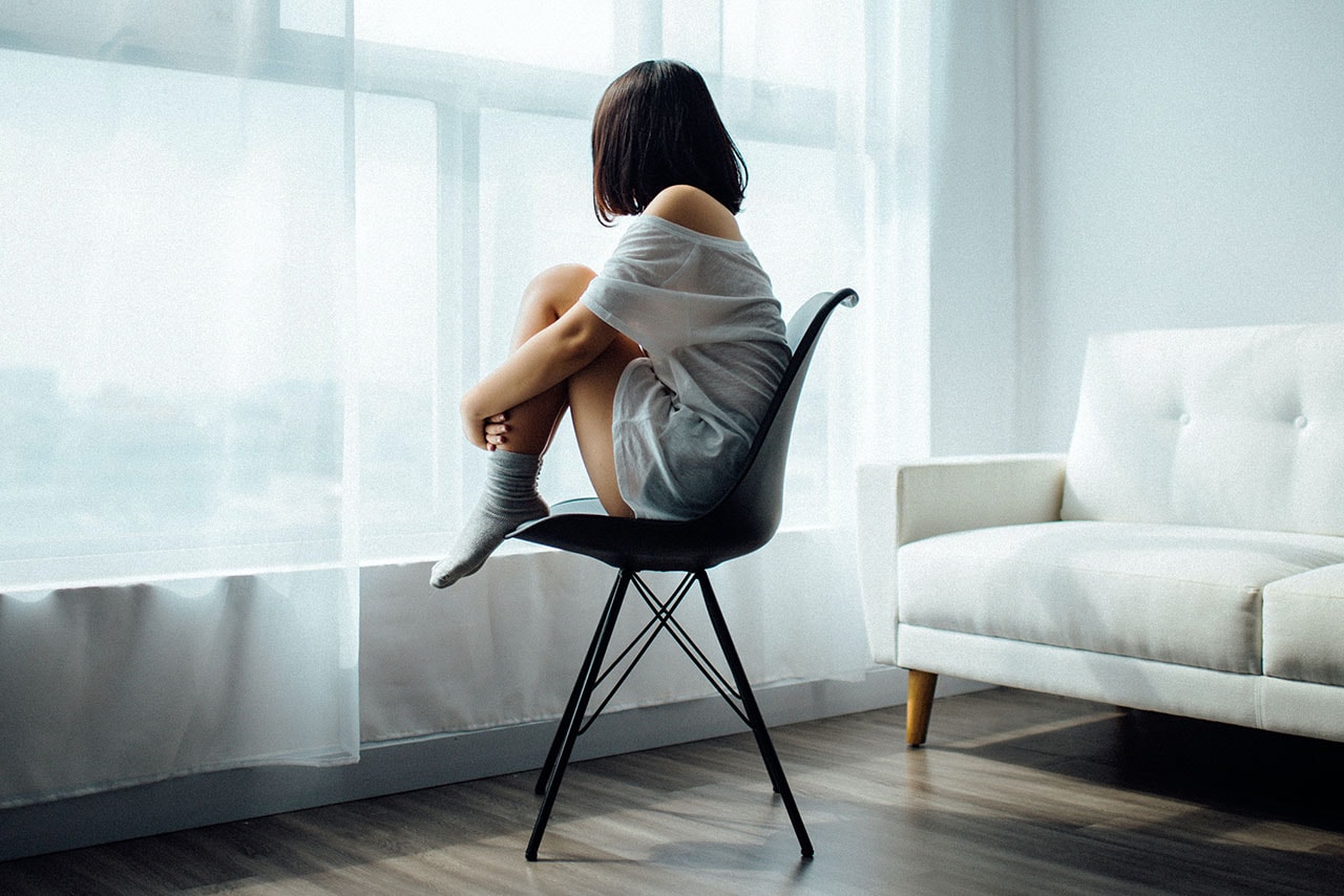 Lonely Woman In White Room Sitting On Chair Glaring Out of Window