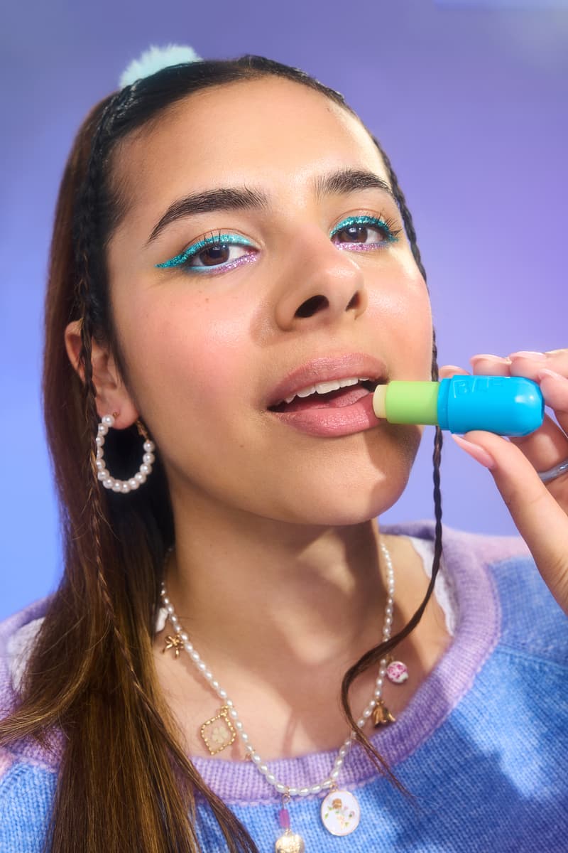 woman with bright blue eyeshadow and ear muffs applying bubble skincare new mint lip balm, beauty, gen-z