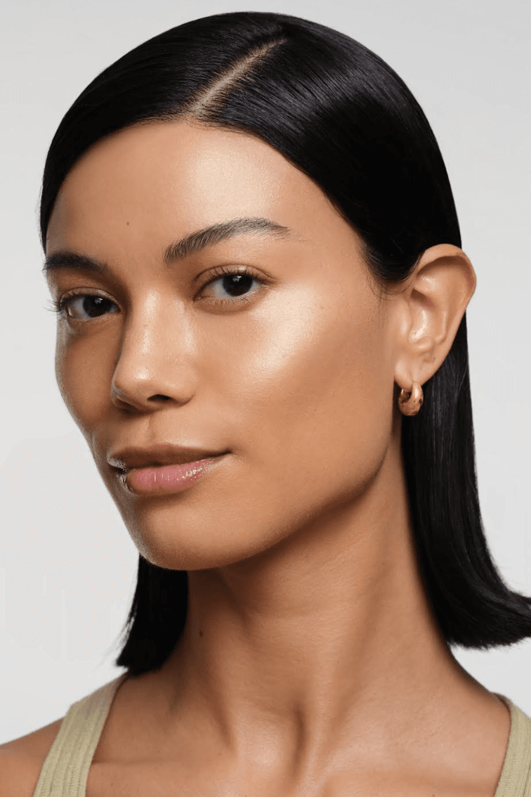 woman caressing bottle of saie beauty glowy super gel in warm glow, swatch of highlighting primer, makeup, skincare