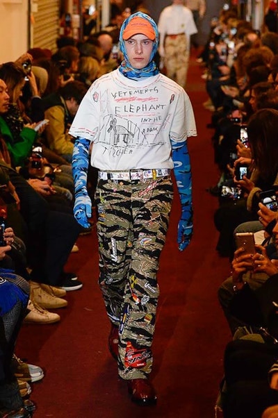 デムナワールドが炸裂した Vetements 2018年秋冬コレクション ストリート＆オーバーサイズという真骨頂の中でスカーフと壊滅的なミリタリーパンツを提案した圧巻のランウェイ パリファッションウィークの公式スケジュールから脱退した〈Vetements（ヴェトモン）〉が、レッドカーペットを敷き詰めた会場で宣言通りの単独ショーを開催した。ストリートとルーズシルエットというDemna Gvasalia（デムナ・ヴァザリア）の真骨頂の中で印象的に映るのは、スカーフの提案と壊滅的に近いミリタリーパンツのダメージ加工。落書きやワッペンの配置、多様多種な柄物のミックスからは、80年代〜90年代のヴィンテージ古着に見るカオティックな雰囲気が漂うほか、Marilyn Manson（マリリン・マンソン）のシャツなども組み込まれ、何とも形容し難いDemnaならではの世界観を構築して観衆を釘付けにした。 ちなみに、下のInstagramの動画はインビテーションであるレシートを撮影したもの。見応え満載の全57体のルックはフォトギャラリーからご確認を。 〈Vetements〉と〈Reebok（リーボック）〉によるブルーを効かせたGenetically Modified Pumpの限定カラーもお買い逃しのないように。