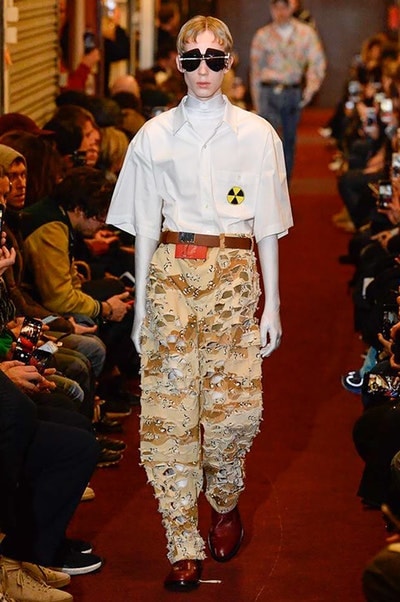 デムナワールドが炸裂した Vetements 2018年秋冬コレクション ストリート＆オーバーサイズという真骨頂の中でスカーフと壊滅的なミリタリーパンツを提案した圧巻のランウェイ パリファッションウィークの公式スケジュールから脱退した〈Vetements（ヴェトモン）〉が、レッドカーペットを敷き詰めた会場で宣言通りの単独ショーを開催した。ストリートとルーズシルエットというDemna Gvasalia（デムナ・ヴァザリア）の真骨頂の中で印象的に映るのは、スカーフの提案と壊滅的に近いミリタリーパンツのダメージ加工。落書きやワッペンの配置、多様多種な柄物のミックスからは、80年代〜90年代のヴィンテージ古着に見るカオティックな雰囲気が漂うほか、Marilyn Manson（マリリン・マンソン）のシャツなども組み込まれ、何とも形容し難いDemnaならではの世界観を構築して観衆を釘付けにした。 ちなみに、下のInstagramの動画はインビテーションであるレシートを撮影したもの。見応え満載の全57体のルックはフォトギャラリーからご確認を。 〈Vetements〉と〈Reebok（リーボック）〉によるブルーを効かせたGenetically Modified Pumpの限定カラーもお買い逃しのないように。