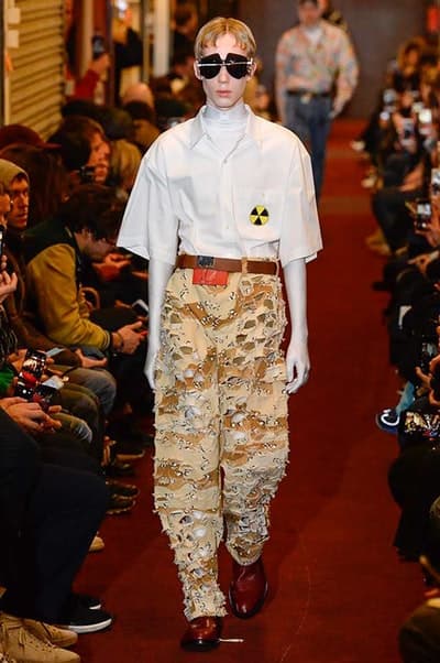 デムナワールドが炸裂した Vetements 2018年秋冬コレクション ストリート&オーバーサイズという真骨頂の中でスカーフと壊滅的なミリタリーパンツを提案した圧巻のランウェイ パリファッションウィークの公式スケジュールから脱退した〈Vetements(ヴェトモン)〉が、レッドカーペットを敷き詰めた会場で宣言通りの単独ショーを開催した。ストリートとルーズシルエットというDemna Gvasalia(デムナ・ヴァザリア)の真骨頂の中で印象的に映るのは、スカーフの提案と壊滅的に近いミリタリーパンツのダメージ加工。落書きやワッペンの配置、多様多種な柄物のミックスからは、80年代〜90年代のヴィンテージ古着に見るカオティックな雰囲気が漂うほか、Marilyn Manson(マリリン・マンソン)のシャツなども組み込まれ、何とも形容し難いDemnaならではの世界観を構築して観衆を釘付けにした。 ちなみに、下のInstagramの動画はインビテーションであるレシートを撮影したもの。見応え満載の全57体のルックはフォトギャラリーからご確認を。 〈Vetements〉と〈Reebok(リーボック)〉によるブルーを効かせたGenetically Modified Pumpの限定カラーもお買い逃しのないように。