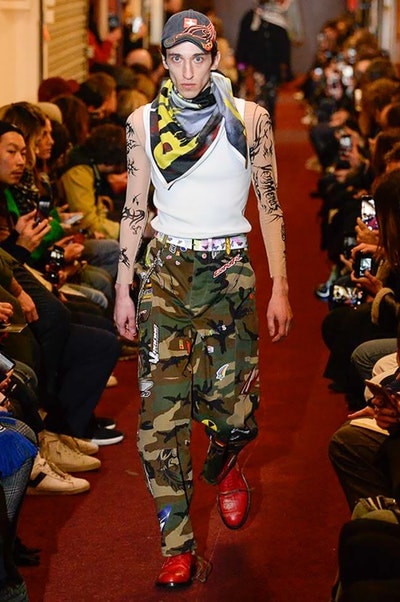 デムナワールドが炸裂した Vetements 2018年秋冬コレクション ストリート＆オーバーサイズという真骨頂の中でスカーフと壊滅的なミリタリーパンツを提案した圧巻のランウェイ パリファッションウィークの公式スケジュールから脱退した〈Vetements（ヴェトモン）〉が、レッドカーペットを敷き詰めた会場で宣言通りの単独ショーを開催した。ストリートとルーズシルエットというDemna Gvasalia（デムナ・ヴァザリア）の真骨頂の中で印象的に映るのは、スカーフの提案と壊滅的に近いミリタリーパンツのダメージ加工。落書きやワッペンの配置、多様多種な柄物のミックスからは、80年代〜90年代のヴィンテージ古着に見るカオティックな雰囲気が漂うほか、Marilyn Manson（マリリン・マンソン）のシャツなども組み込まれ、何とも形容し難いDemnaならではの世界観を構築して観衆を釘付けにした。 ちなみに、下のInstagramの動画はインビテーションであるレシートを撮影したもの。見応え満載の全57体のルックはフォトギャラリーからご確認を。 〈Vetements〉と〈Reebok（リーボック）〉によるブルーを効かせたGenetically Modified Pumpの限定カラーもお買い逃しのないように。