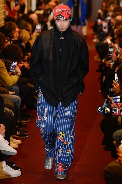デムナワールドが炸裂した Vetements 2018年秋冬コレクション ストリート＆オーバーサイズという真骨頂の中でスカーフと壊滅的なミリタリーパンツを提案した圧巻のランウェイ パリファッションウィークの公式スケジュールから脱退した〈Vetements（ヴェトモン）〉が、レッドカーペットを敷き詰めた会場で宣言通りの単独ショーを開催した。ストリートとルーズシルエットというDemna Gvasalia（デムナ・ヴァザリア）の真骨頂の中で印象的に映るのは、スカーフの提案と壊滅的に近いミリタリーパンツのダメージ加工。落書きやワッペンの配置、多様多種な柄物のミックスからは、80年代〜90年代のヴィンテージ古着に見るカオティックな雰囲気が漂うほか、Marilyn Manson（マリリン・マンソン）のシャツなども組み込まれ、何とも形容し難いDemnaならではの世界観を構築して観衆を釘付けにした。 ちなみに、下のInstagramの動画はインビテーションであるレシートを撮影したもの。見応え満載の全57体のルックはフォトギャラリーからご確認を。 〈Vetements〉と〈Reebok（リーボック）〉によるブルーを効かせたGenetically Modified Pumpの限定カラーもお買い逃しのないように。