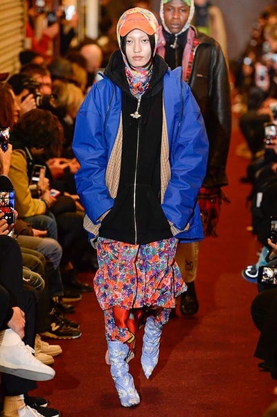 デムナワールドが炸裂した Vetements 2018年秋冬コレクション ストリート＆オーバーサイズという真骨頂の中でスカーフと壊滅的なミリタリーパンツを提案した圧巻のランウェイ パリファッションウィークの公式スケジュールから脱退した〈Vetements（ヴェトモン）〉が、レッドカーペットを敷き詰めた会場で宣言通りの単独ショーを開催した。ストリートとルーズシルエットというDemna Gvasalia（デムナ・ヴァザリア）の真骨頂の中で印象的に映るのは、スカーフの提案と壊滅的に近いミリタリーパンツのダメージ加工。落書きやワッペンの配置、多様多種な柄物のミックスからは、80年代〜90年代のヴィンテージ古着に見るカオティックな雰囲気が漂うほか、Marilyn Manson（マリリン・マンソン）のシャツなども組み込まれ、何とも形容し難いDemnaならではの世界観を構築して観衆を釘付けにした。 ちなみに、下のInstagramの動画はインビテーションであるレシートを撮影したもの。見応え満載の全57体のルックはフォトギャラリーからご確認を。 〈Vetements〉と〈Reebok（リーボック）〉によるブルーを効かせたGenetically Modified Pumpの限定カラーもお買い逃しのないように。