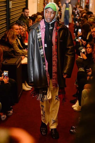 デムナワールドが炸裂した Vetements 2018年秋冬コレクション ストリート&オーバーサイズという真骨頂の中でスカーフと壊滅的なミリタリーパンツを提案した圧巻のランウェイ パリファッションウィークの公式スケジュールから脱退した〈Vetements(ヴェトモン)〉が、レッドカーペットを敷き詰めた会場で宣言通りの単独ショーを開催した。ストリートとルーズシルエットというDemna Gvasalia(デムナ・ヴァザリア)の真骨頂の中で印象的に映るのは、スカーフの提案と壊滅的に近いミリタリーパンツのダメージ加工。落書きやワッペンの配置、多様多種な柄物のミックスからは、80年代〜90年代のヴィンテージ古着に見るカオティックな雰囲気が漂うほか、Marilyn Manson(マリリン・マンソン)のシャツなども組み込まれ、何とも形容し難いDemnaならではの世界観を構築して観衆を釘付けにした。 ちなみに、下のInstagramの動画はインビテーションであるレシートを撮影したもの。見応え満載の全57体のルックはフォトギャラリーからご確認を。 〈Vetements〉と〈Reebok(リーボック)〉によるブルーを効かせたGenetically Modified Pumpの限定カラーもお買い逃しのないように。