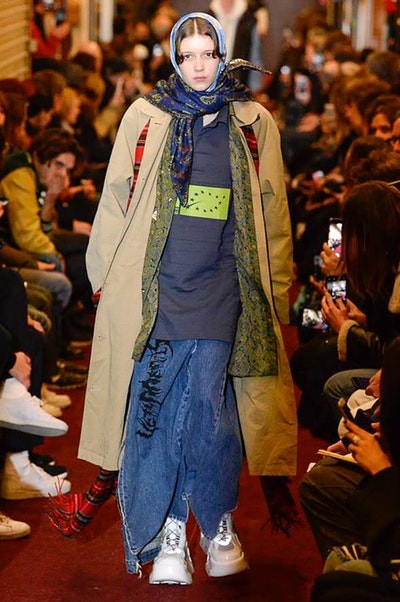 デムナワールドが炸裂した Vetements 2018年秋冬コレクション ストリート＆オーバーサイズという真骨頂の中でスカーフと壊滅的なミリタリーパンツを提案した圧巻のランウェイ パリファッションウィークの公式スケジュールから脱退した〈Vetements（ヴェトモン）〉が、レッドカーペットを敷き詰めた会場で宣言通りの単独ショーを開催した。ストリートとルーズシルエットというDemna Gvasalia（デムナ・ヴァザリア）の真骨頂の中で印象的に映るのは、スカーフの提案と壊滅的に近いミリタリーパンツのダメージ加工。落書きやワッペンの配置、多様多種な柄物のミックスからは、80年代〜90年代のヴィンテージ古着に見るカオティックな雰囲気が漂うほか、Marilyn Manson（マリリン・マンソン）のシャツなども組み込まれ、何とも形容し難いDemnaならではの世界観を構築して観衆を釘付けにした。 ちなみに、下のInstagramの動画はインビテーションであるレシートを撮影したもの。見応え満載の全57体のルックはフォトギャラリーからご確認を。 〈Vetements〉と〈Reebok（リーボック）〉によるブルーを効かせたGenetically Modified Pumpの限定カラーもお買い逃しのないように。