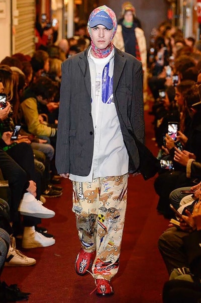 デムナワールドが炸裂した Vetements 2018年秋冬コレクション ストリート＆オーバーサイズという真骨頂の中でスカーフと壊滅的なミリタリーパンツを提案した圧巻のランウェイ パリファッションウィークの公式スケジュールから脱退した〈Vetements（ヴェトモン）〉が、レッドカーペットを敷き詰めた会場で宣言通りの単独ショーを開催した。ストリートとルーズシルエットというDemna Gvasalia（デムナ・ヴァザリア）の真骨頂の中で印象的に映るのは、スカーフの提案と壊滅的に近いミリタリーパンツのダメージ加工。落書きやワッペンの配置、多様多種な柄物のミックスからは、80年代〜90年代のヴィンテージ古着に見るカオティックな雰囲気が漂うほか、Marilyn Manson（マリリン・マンソン）のシャツなども組み込まれ、何とも形容し難いDemnaならではの世界観を構築して観衆を釘付けにした。 ちなみに、下のInstagramの動画はインビテーションであるレシートを撮影したもの。見応え満載の全57体のルックはフォトギャラリーからご確認を。 〈Vetements〉と〈Reebok（リーボック）〉によるブルーを効かせたGenetically Modified Pumpの限定カラーもお買い逃しのないように。