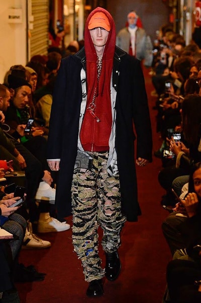 デムナワールドが炸裂した Vetements 2018年秋冬コレクション ストリート＆オーバーサイズという真骨頂の中でスカーフと壊滅的なミリタリーパンツを提案した圧巻のランウェイ パリファッションウィークの公式スケジュールから脱退した〈Vetements（ヴェトモン）〉が、レッドカーペットを敷き詰めた会場で宣言通りの単独ショーを開催した。ストリートとルーズシルエットというDemna Gvasalia（デムナ・ヴァザリア）の真骨頂の中で印象的に映るのは、スカーフの提案と壊滅的に近いミリタリーパンツのダメージ加工。落書きやワッペンの配置、多様多種な柄物のミックスからは、80年代〜90年代のヴィンテージ古着に見るカオティックな雰囲気が漂うほか、Marilyn Manson（マリリン・マンソン）のシャツなども組み込まれ、何とも形容し難いDemnaならではの世界観を構築して観衆を釘付けにした。 ちなみに、下のInstagramの動画はインビテーションであるレシートを撮影したもの。見応え満載の全57体のルックはフォトギャラリーからご確認を。 〈Vetements〉と〈Reebok（リーボック）〉によるブルーを効かせたGenetically Modified Pumpの限定カラーもお買い逃しのないように。