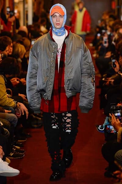 デムナワールドが炸裂した Vetements 2018年秋冬コレクション ストリート&オーバーサイズという真骨頂の中でスカーフと壊滅的なミリタリーパンツを提案した圧巻のランウェイ パリファッションウィークの公式スケジュールから脱退した〈Vetements(ヴェトモン)〉が、レッドカーペットを敷き詰めた会場で宣言通りの単独ショーを開催した。ストリートとルーズシルエットというDemna Gvasalia(デムナ・ヴァザリア)の真骨頂の中で印象的に映るのは、スカーフの提案と壊滅的に近いミリタリーパンツのダメージ加工。落書きやワッペンの配置、多様多種な柄物のミックスからは、80年代〜90年代のヴィンテージ古着に見るカオティックな雰囲気が漂うほか、Marilyn Manson(マリリン・マンソン)のシャツなども組み込まれ、何とも形容し難いDemnaならではの世界観を構築して観衆を釘付けにした。 ちなみに、下のInstagramの動画はインビテーションであるレシートを撮影したもの。見応え満載の全57体のルックはフォトギャラリーからご確認を。 〈Vetements〉と〈Reebok(リーボック)〉によるブルーを効かせたGenetically Modified Pumpの限定カラーもお買い逃しのないように。