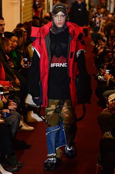 デムナワールドが炸裂した Vetements 2018年秋冬コレクション ストリート&オーバーサイズという真骨頂の中でスカーフと壊滅的なミリタリーパンツを提案した圧巻のランウェイ パリファッションウィークの公式スケジュールから脱退した〈Vetements(ヴェトモン)〉が、レッドカーペットを敷き詰めた会場で宣言通りの単独ショーを開催した。ストリートとルーズシルエットというDemna Gvasalia(デムナ・ヴァザリア)の真骨頂の中で印象的に映るのは、スカーフの提案と壊滅的に近いミリタリーパンツのダメージ加工。落書きやワッペンの配置、多様多種な柄物のミックスからは、80年代〜90年代のヴィンテージ古着に見るカオティックな雰囲気が漂うほか、Marilyn Manson(マリリン・マンソン)のシャツなども組み込まれ、何とも形容し難いDemnaならではの世界観を構築して観衆を釘付けにした。 ちなみに、下のInstagramの動画はインビテーションであるレシートを撮影したもの。見応え満載の全57体のルックはフォトギャラリーからご確認を。 〈Vetements〉と〈Reebok(リーボック)〉によるブルーを効かせたGenetically Modified Pumpの限定カラーもお買い逃しのないように。