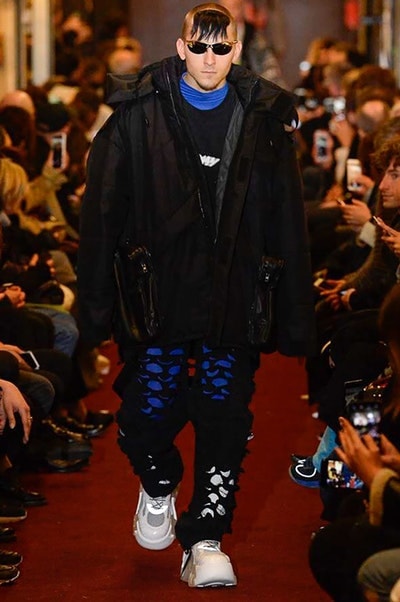 デムナワールドが炸裂した Vetements 2018年秋冬コレクション ストリート＆オーバーサイズという真骨頂の中でスカーフと壊滅的なミリタリーパンツを提案した圧巻のランウェイ パリファッションウィークの公式スケジュールから脱退した〈Vetements（ヴェトモン）〉が、レッドカーペットを敷き詰めた会場で宣言通りの単独ショーを開催した。ストリートとルーズシルエットというDemna Gvasalia（デムナ・ヴァザリア）の真骨頂の中で印象的に映るのは、スカーフの提案と壊滅的に近いミリタリーパンツのダメージ加工。落書きやワッペンの配置、多様多種な柄物のミックスからは、80年代〜90年代のヴィンテージ古着に見るカオティックな雰囲気が漂うほか、Marilyn Manson（マリリン・マンソン）のシャツなども組み込まれ、何とも形容し難いDemnaならではの世界観を構築して観衆を釘付けにした。 ちなみに、下のInstagramの動画はインビテーションであるレシートを撮影したもの。見応え満載の全57体のルックはフォトギャラリーからご確認を。 〈Vetements〉と〈Reebok（リーボック）〉によるブルーを効かせたGenetically Modified Pumpの限定カラーもお買い逃しのないように。