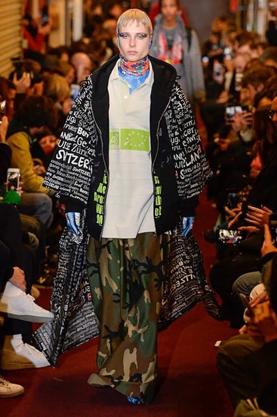 デムナワールドが炸裂した Vetements 2018年秋冬コレクション ストリート＆オーバーサイズという真骨頂の中でスカーフと壊滅的なミリタリーパンツを提案した圧巻のランウェイ パリファッションウィークの公式スケジュールから脱退した〈Vetements（ヴェトモン）〉が、レッドカーペットを敷き詰めた会場で宣言通りの単独ショーを開催した。ストリートとルーズシルエットというDemna Gvasalia（デムナ・ヴァザリア）の真骨頂の中で印象的に映るのは、スカーフの提案と壊滅的に近いミリタリーパンツのダメージ加工。落書きやワッペンの配置、多様多種な柄物のミックスからは、80年代〜90年代のヴィンテージ古着に見るカオティックな雰囲気が漂うほか、Marilyn Manson（マリリン・マンソン）のシャツなども組み込まれ、何とも形容し難いDemnaならではの世界観を構築して観衆を釘付けにした。 ちなみに、下のInstagramの動画はインビテーションであるレシートを撮影したもの。見応え満載の全57体のルックはフォトギャラリーからご確認を。 〈Vetements〉と〈Reebok（リーボック）〉によるブルーを効かせたGenetically Modified Pumpの限定カラーもお買い逃しのないように。