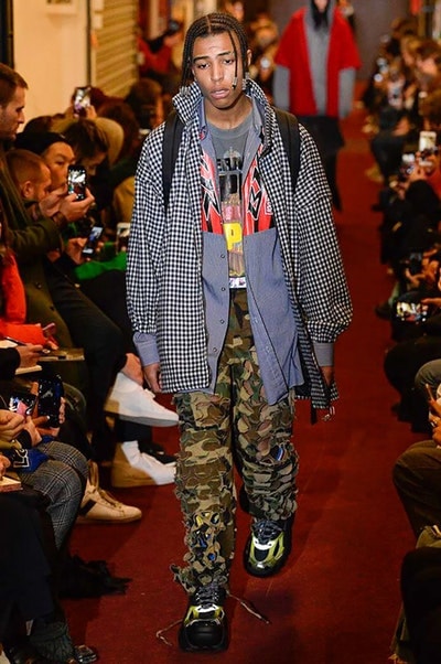 デムナワールドが炸裂した Vetements 2018年秋冬コレクション ストリート＆オーバーサイズという真骨頂の中でスカーフと壊滅的なミリタリーパンツを提案した圧巻のランウェイ パリファッションウィークの公式スケジュールから脱退した〈Vetements（ヴェトモン）〉が、レッドカーペットを敷き詰めた会場で宣言通りの単独ショーを開催した。ストリートとルーズシルエットというDemna Gvasalia（デムナ・ヴァザリア）の真骨頂の中で印象的に映るのは、スカーフの提案と壊滅的に近いミリタリーパンツのダメージ加工。落書きやワッペンの配置、多様多種な柄物のミックスからは、80年代〜90年代のヴィンテージ古着に見るカオティックな雰囲気が漂うほか、Marilyn Manson（マリリン・マンソン）のシャツなども組み込まれ、何とも形容し難いDemnaならではの世界観を構築して観衆を釘付けにした。 ちなみに、下のInstagramの動画はインビテーションであるレシートを撮影したもの。見応え満載の全57体のルックはフォトギャラリーからご確認を。 〈Vetements〉と〈Reebok（リーボック）〉によるブルーを効かせたGenetically Modified Pumpの限定カラーもお買い逃しのないように。