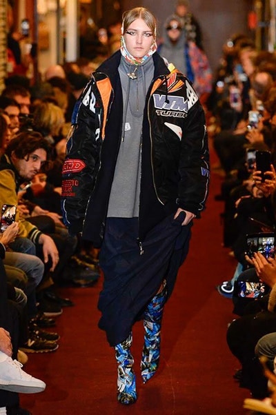 デムナワールドが炸裂した Vetements 2018年秋冬コレクション ストリート＆オーバーサイズという真骨頂の中でスカーフと壊滅的なミリタリーパンツを提案した圧巻のランウェイ パリファッションウィークの公式スケジュールから脱退した〈Vetements（ヴェトモン）〉が、レッドカーペットを敷き詰めた会場で宣言通りの単独ショーを開催した。ストリートとルーズシルエットというDemna Gvasalia（デムナ・ヴァザリア）の真骨頂の中で印象的に映るのは、スカーフの提案と壊滅的に近いミリタリーパンツのダメージ加工。落書きやワッペンの配置、多様多種な柄物のミックスからは、80年代〜90年代のヴィンテージ古着に見るカオティックな雰囲気が漂うほか、Marilyn Manson（マリリン・マンソン）のシャツなども組み込まれ、何とも形容し難いDemnaならではの世界観を構築して観衆を釘付けにした。 ちなみに、下のInstagramの動画はインビテーションであるレシートを撮影したもの。見応え満載の全57体のルックはフォトギャラリーからご確認を。 〈Vetements〉と〈Reebok（リーボック）〉によるブルーを効かせたGenetically Modified Pumpの限定カラーもお買い逃しのないように。