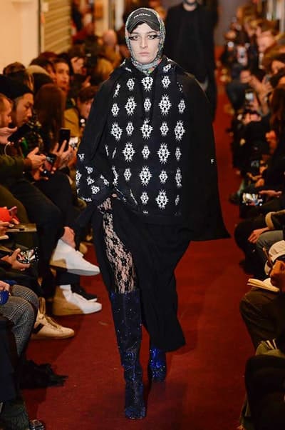 デムナワールドが炸裂した Vetements 2018年秋冬コレクション ストリート&オーバーサイズという真骨頂の中でスカーフと壊滅的なミリタリーパンツを提案した圧巻のランウェイ パリファッションウィークの公式スケジュールから脱退した〈Vetements(ヴェトモン)〉が、レッドカーペットを敷き詰めた会場で宣言通りの単独ショーを開催した。ストリートとルーズシルエットというDemna Gvasalia(デムナ・ヴァザリア)の真骨頂の中で印象的に映るのは、スカーフの提案と壊滅的に近いミリタリーパンツのダメージ加工。落書きやワッペンの配置、多様多種な柄物のミックスからは、80年代〜90年代のヴィンテージ古着に見るカオティックな雰囲気が漂うほか、Marilyn Manson(マリリン・マンソン)のシャツなども組み込まれ、何とも形容し難いDemnaならではの世界観を構築して観衆を釘付けにした。 ちなみに、下のInstagramの動画はインビテーションであるレシートを撮影したもの。見応え満載の全57体のルックはフォトギャラリーからご確認を。 〈Vetements〉と〈Reebok(リーボック)〉によるブルーを効かせたGenetically Modified Pumpの限定カラーもお買い逃しのないように。