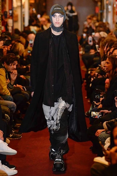 デムナワールドが炸裂した Vetements 2018年秋冬コレクション ストリート＆オーバーサイズという真骨頂の中でスカーフと壊滅的なミリタリーパンツを提案した圧巻のランウェイ パリファッションウィークの公式スケジュールから脱退した〈Vetements（ヴェトモン）〉が、レッドカーペットを敷き詰めた会場で宣言通りの単独ショーを開催した。ストリートとルーズシルエットというDemna Gvasalia（デムナ・ヴァザリア）の真骨頂の中で印象的に映るのは、スカーフの提案と壊滅的に近いミリタリーパンツのダメージ加工。落書きやワッペンの配置、多様多種な柄物のミックスからは、80年代〜90年代のヴィンテージ古着に見るカオティックな雰囲気が漂うほか、Marilyn Manson（マリリン・マンソン）のシャツなども組み込まれ、何とも形容し難いDemnaならではの世界観を構築して観衆を釘付けにした。 ちなみに、下のInstagramの動画はインビテーションであるレシートを撮影したもの。見応え満載の全57体のルックはフォトギャラリーからご確認を。 〈Vetements〉と〈Reebok（リーボック）〉によるブルーを効かせたGenetically Modified Pumpの限定カラーもお買い逃しのないように。
