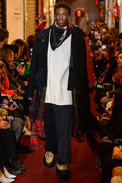 デムナワールドが炸裂した Vetements 2018年秋冬コレクション ストリート＆オーバーサイズという真骨頂の中でスカーフと壊滅的なミリタリーパンツを提案した圧巻のランウェイ パリファッションウィークの公式スケジュールから脱退した〈Vetements（ヴェトモン）〉が、レッドカーペットを敷き詰めた会場で宣言通りの単独ショーを開催した。ストリートとルーズシルエットというDemna Gvasalia（デムナ・ヴァザリア）の真骨頂の中で印象的に映るのは、スカーフの提案と壊滅的に近いミリタリーパンツのダメージ加工。落書きやワッペンの配置、多様多種な柄物のミックスからは、80年代〜90年代のヴィンテージ古着に見るカオティックな雰囲気が漂うほか、Marilyn Manson（マリリン・マンソン）のシャツなども組み込まれ、何とも形容し難いDemnaならではの世界観を構築して観衆を釘付けにした。 ちなみに、下のInstagramの動画はインビテーションであるレシートを撮影したもの。見応え満載の全57体のルックはフォトギャラリーからご確認を。 〈Vetements〉と〈Reebok（リーボック）〉によるブルーを効かせたGenetically Modified Pumpの限定カラーもお買い逃しのないように。
