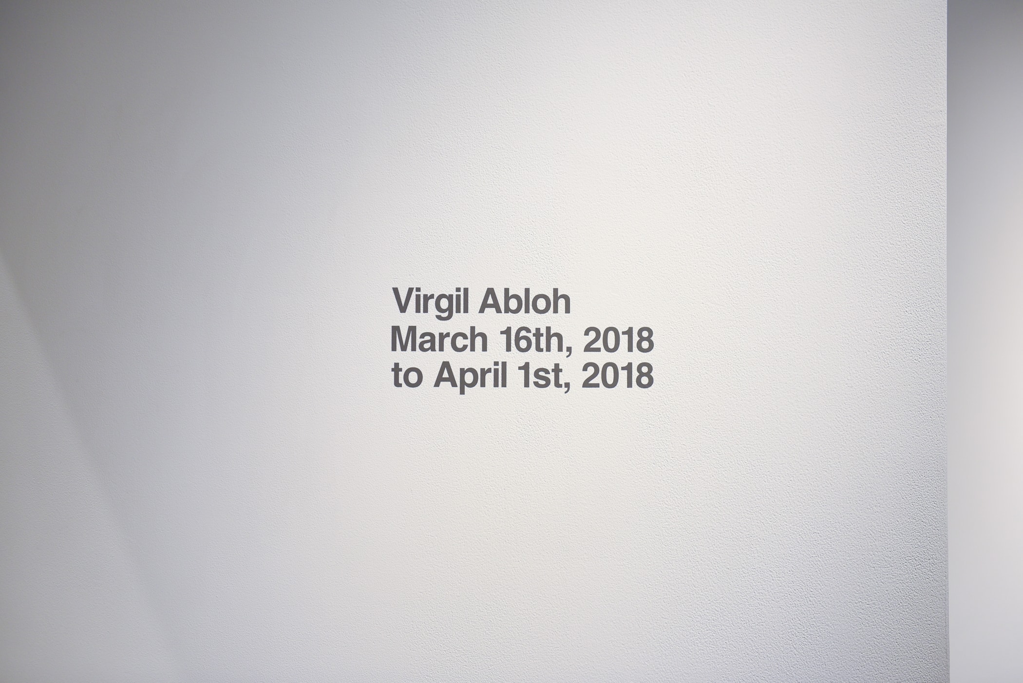 ヴァージル・アブロー初の個展 “PAY PER VIEW” に潜入 メディアや広告に踊らされ、消費によって形作られる現代社会へ向けた異才からのメッセージを体感せよ 良くも悪くもメディアや広告に踊らされ、消費によって形作られる現代社会へ向けた異才からのメッセージ 3月16日（金）より、『Kaikai Kiki Gallery』ではVirgil Abloh（ヴァージル・アブロー）の個展“PAY PER VIEW”が開催されている。「俺たちは全員、消費という行為によって形作られている」、そんなキャッチコピーを掲げる本展では、メディアが人類による世界の見方にいかに重大な影響を与えているのかを示すものだ。  ひとつめの部屋の中央には、モーターレース「NASCAR（ナスカー）」の公式スポンサーである石油会社「SUNOCO（スノコ）」の脚の折れたガソリンスタンド看板が鎮座。また、そのアートピースを背にした正面には、「“ADVERTISE HERE”」の文字が書かれたキャンバスが設置されているが、その下に添えられている電話番号「+1-855-633-9483」はVirgil本人のTwitterにも記載があり、実際にここに電話をかけると〈Off-White™️（オフホワイト）〉のデザイナーが2016年春のコレクション“Blue Collar”の説明をしてくれるのだ。また、ローラーなどは一切使用せず、黒い油絵具と画筆で塗り潰された3,000cm x 1,000cmのキャンバスは、戦前に抽象絵画を手掛けた最初の人物、Kasimir Malevich（カジミール・マレーヴィチ）の作品「黒の正方形」にインスパイアされている。美術史に大きな足跡を残し、存在論や認識論など様々な角度から分析されたこの名画は、視覚的刺激や意味をなすものを排除した完全なる抽象画であるが、Virgilが一人で描き上げたキャンバスの下には、「JCDecaux（ジーセードコー）」、「OUTFRONT（アウトフロント）」、「LAMAR（ラマー）」といった広告企業のロゴが配置。VirgilはMalevichの対話のルールを使って線と線をつなぎ、鑑賞者は広告が持つ力を突き詰めて蒸留したところに残る核心である、という内在的な意図を解き明かしているのだ。  一方、奥の部屋は床一面が畳に。中央に置かれたサイネージに流れてるのは、バルセロナで撮影した〈Off-White™️〉のコレクションムービーだが、「Coca-Cola（コカ・コーラ）」、「DASANI（ダサニ）」、「Perrier（ペリエ）」など、世界的知名度を持つ飲料のロゴを表示するアナログな作品と、スプレーペイントを施した4枚綴りのキャンバスが同居することにより、言葉にしがたい不思議な感覚に陥る空間のミスマッチが生じている。  “PAY PER VIEW”の展示の様子は上のフォトギャラリーよりご確認いただけるが、作品を俯瞰で捉え、感覚を研ぎ澄ますことで伝わってくるVirgilのメッセージはこの空間でしか感じることができない。以下の会期とご自身のスケジュールを照らし合わせ、是非『Kaikai Kiki Gallery』まで足を運んでみてはいかがだろうか。  Virgil Abloh “PAY PER VIEW” @ Kaikai Kiki Gallery 住所：東京都港区元麻布2-3-30 元麻布クレストビルB1 会期：2018年3月16日（金）〜4月1日（日） 時間：11:00 – 19:00 休館日：日、月、祝（最終日の4月1日のみ日曜営業）