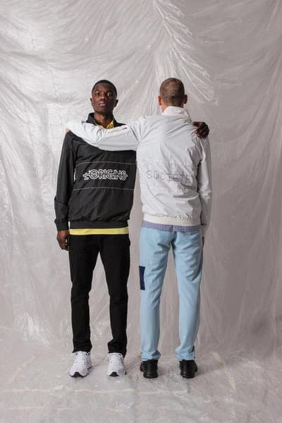 ガーナ発の L’ORIGINE よりシンプルな中にも強いメッセージ性を持った2018年夏コレクションが到着 肌の色の違うモデルや補色を使ったアイテムで人種や民族による隔たりのないオープンな社会を表現 2014年に設立されたガーナ発の新鋭ブランド〈L’ORIGINE（ロリジンヌ）〉が2017年秋冬コレクションに続き、クリーンさが際立つトップスやボトムスから小物類までを網羅した2018年サマーコレクションを発表。  二人のデザイナー、Dyllan Ahinful（ディラン・アヒンフル）とJeffrey Mensah（ジェフリー・メンサー）が率いる同ブランドであるが、今季は“Opposites Attract And Enhance”をテーマとして相違点にフォーカス。肌の色の違う二人のモデルを起用し、補色（互いの色を最も目立たせる色の組み合わせ）を強調することで、性質の異なるものが一緒になり生まれる相乗効果を表わしている。また、カラースキームにおいては、Claude Monet（クロード・モネ）らに代表される印象派にインスパイアされており、パステルブルーとイエローを基調としたアイテムが全ルックに登場、ミニマルな装飾が施されたポロシャツからショーツ、トラックスーツまでが並ぶ。その他にはストライプ柄のシャツや、ベーシックなブラックとホワイトをベースにブランドロゴなどのグラフィックがプリントされたフーディーやナイロン素材のアノラック、ボディバッグやサンダルがラインアップ。  今サマーコレクションは、〈L’ORIGINE〉の公式サイトにて一部のアイテムのプレオーダーを開始している。まずは上のフォトロールより、デザイナーのメッセージが詰まった各ルックをチェックしてみよう。