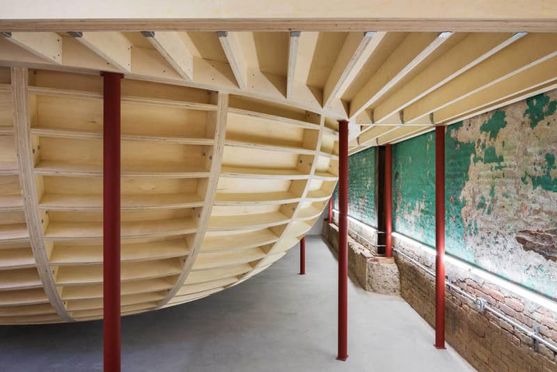 Supreme のブルックリン店の内装デザインを隅々まで撮影したフォトセットが到着 『Supreme Brooklyn』の前は配送用トラックの収納スペースだったとのこと 〈Supreme（シュプリーム）〉は昨年10月、ニューヨーク・ブルックリン地区に新ストアをオープン。実はこの場所、ストリートウェアの雄のためにNeil Logan（ニール・ローガン）とMinji Kim（ミンジ・キム）の2人が改装する前は、2,938㎡を要する配送用トラックの収納スペースだったのだ。  天井が高く、しっくりを剥がした2m超えのブロック壁に囲まれた空間は、隆起したグラインドレール付きのメタルベンチを設置することで、質素ながらもどこかインダストリアルな雰囲気が漂う。また、店内の奥には『Supreme Brooklyn』の最大の特徴である木製のスケートボウルが鎮座。『ArchDaily』はこのアイコンについて、「バルト海産の樺の木でできたベニヤ板を100%使用したこのボウルは、アートコレクティブのSimparchがシカゴで製造して、ここまで運び、インストールしたものです」と説明している。  また、このジオメトリックなボウルの裏には、カーテンで覆われた更衣室が2部屋隠れており、スケートクリップを流している店頭の液晶も背面には鏡を設置。そして、入り口の壁裏を覆い尽くすスケートデッキとアートワークも見逃せないポイントだろう。  『Supreme Brooklyn』の内装を隅々まで撮影したフォトセットは、上のフォトギャラリーからどうぞ。  ちなみに、〈Sup〉が2018年春夏コレクション内の“Alphabet”シリーズの販売を突如中止した理由はご存知？