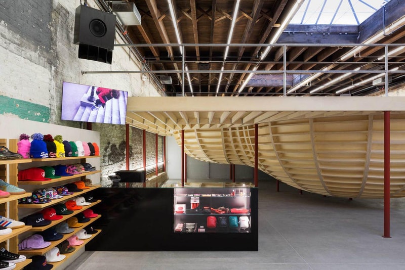 Supreme のブルックリン店の内装デザインを隅々まで撮影したフォトセットが到着 『Supreme Brooklyn』の前は配送用トラックの収納スペースだったとのこと 〈Supreme（シュプリーム）〉は昨年10月、ニューヨーク・ブルックリン地区に新ストアをオープン。実はこの場所、ストリートウェアの雄のためにNeil Logan（ニール・ローガン）とMinji Kim（ミンジ・キム）の2人が改装する前は、2,938㎡を要する配送用トラックの収納スペースだったのだ。  天井が高く、しっくりを剥がした2m超えのブロック壁に囲まれた空間は、隆起したグラインドレール付きのメタルベンチを設置することで、質素ながらもどこかインダストリアルな雰囲気が漂う。また、店内の奥には『Supreme Brooklyn』の最大の特徴である木製のスケートボウルが鎮座。『ArchDaily』はこのアイコンについて、「バルト海産の樺の木でできたベニヤ板を100%使用したこのボウルは、アートコレクティブのSimparchがシカゴで製造して、ここまで運び、インストールしたものです」と説明している。  また、このジオメトリックなボウルの裏には、カーテンで覆われた更衣室が2部屋隠れており、スケートクリップを流している店頭の液晶も背面には鏡を設置。そして、入り口の壁裏を覆い尽くすスケートデッキとアートワークも見逃せないポイントだろう。  『Supreme Brooklyn』の内装を隅々まで撮影したフォトセットは、上のフォトギャラリーからどうぞ。  ちなみに、〈Sup〉が2018年春夏コレクション内の“Alphabet”シリーズの販売を突如中止した理由はご存知？