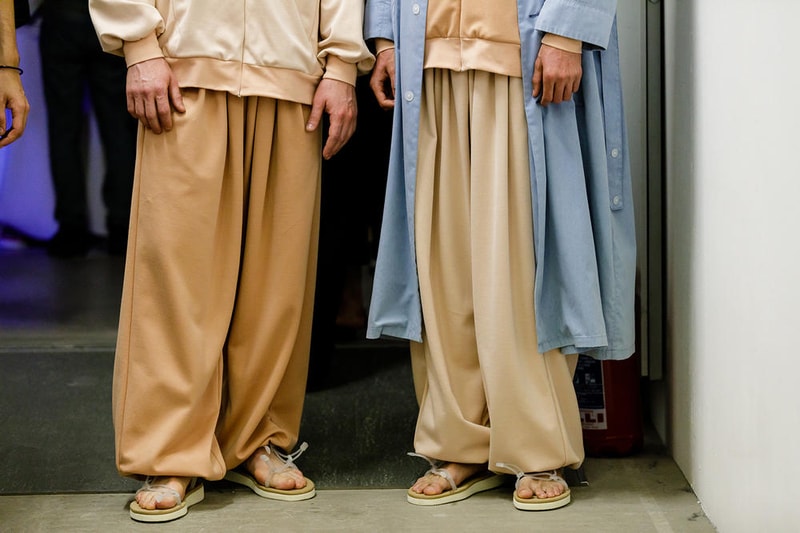 丸龍文人の帰還は、2019年春夏シーズン最大のトピックのひとつだった。〈COMME des GARÇONS（コム デ ギャルソン）〉退社から約2年の時を経て、同氏は自身の名を冠した〈FUMITO GANRYU（フミト ガンリュー）〉を「Pitti Uomo（ピッティ ウォモ）」の“Designer Project”で発表。幸運にも、『HYPEBEAST』はこの新たな船出となるランウェイの舞台裏に潜入する機会を得ることができた。  1stコレクションに言及する前に、〈GANRYU〉の時代を振り返ってみたい。シャツ、デニム、テーラードジャケットなど、ベースとなるカジュアルウェアは決して新鮮味を感じるものではない。だが、丸龍氏の手にかかれば、それらの洋服はモードに寄っていくのではなく、文字通り“昇華”されてしまうのだ。かつて『Union（ユニオン）』のChris Gibbs（クリス・ギブス）も「COMME des GARÇONSファミリーの中で最も完璧なブランドだ。なぜなら、GANRYUはストリートウェア、ワークウェア、ハイファッションを融合しているからである」と『BoF』の中で同氏のクリエイションを手放しに賞賛。それだけ、〈GANRYU〉はどこよりも早く、ランウェイからストリートにリーチしていたのだ。  〈FUMITO GANRYU〉のデビューコレクションは、会場に水の逆光写真が飾られた空間でお披露目を迎えた。ランウェイでは極限までクリーンに仕立てられたスポーツウェアが随所で登場し、カトリックの衣装を彷彿とさせるオーバーサイズのフーディや半透明のクリアベルトを採用したサンダルがキーピースに。そのシルエット美には誰しもが「シーンに丸龍文人が帰ってきた」と感じたことだろう。  〈FUMITO GANRYU〉初のコレクションの細部に迫るバックステージフォトは、上のフォトギャラリーから。取扱店舗などの詳細は、@fumitoganryuなどを含め、ブランドからのアップデートを待とう。  あわせて、先日閉幕したロンドンファッションウィーク・メンズ期間中に敢行したストリートスナップもお見逃しなく。