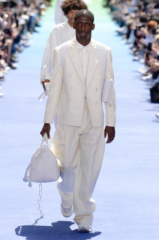 ヴァージル・アブローが手がけた Louis Vuitton 2019年春夏コレクションが遂にお披露目 ファッション界に後世まで語り継がれる歴史的1ページが追加される 〈Louis Vuitton(ルイ ヴィトン)〉がVirgil Abloh(ヴァージル・アブロー)のアーティスティック・ディレクター就任を発表してから早3ヶ月、遂に今をときめくデザイナーの〈LV〉デビューとなる2019年春夏コレクションがお披露目を迎えた。 晴天のパレ・ロワイヤル庭園には、Kanye West(カニエ・ウェスト)とその妻Kim Kardashian(キム・カーダシアン)や、Rihanna(リアーナ)、Kylie Jenner(カイリー・ジェンナー)、A$AP Rocky(エイサップ・ロッキー)、村上隆など、Virgilの友人でもある豪華ゲストが集結。ヒップホップとジャズを繋ぐ成長著しいカルテット、BadBadNotGood(バッドバッドノットグッド)がサウンドトラックを提供したランウェイには、Kid Cudi(キッド・カディ)、Dev Hynes(デヴ・ハインズ)、A$AP Nast(エイサップ・ナスト)、Playboi Carti(プレイボーイ・カルティ)、Theophilus London(テオフィルス・ロンドン)、そして〈Palace(パレス)〉よりLucien Clarke(ルシアン・クラーク)とBlondey McCoy(ブロンディ・マッコイ)らがモデルに起用された。 全56体のルックでは、〈Off-White™️(オフホワイト)〉の党首の真髄である“ラグジュアリーとストリートの融合”が力強さとともに解き放たれた。タイダイ、フローラルパターン、来年80周年を迎える映画『オズの魔法使い』とのコラボレーションなど、必要最小限でありながらも視覚的魅力を放つアイテムがコレクションにエンターテイメント性を付与し、ドラマチックな雰囲気を醸すそのランウェイでは、ルーズフィットのパンツやユーティリティベスト、シアーシャツ、フーディ、仕立ての良いトレンチコートなどがカラーパレットごとに紹介されていく。また、昨日Virgil本人が先行公開したバスケットシューズ風の一足を含め、フットウェアはハイトップシルエットを中心に構成され、上質なドレスシューズもシューレースの配色で遊びをプラス。加えて、〈Louis Vuitton〉の象徴とも言えるラゲージ類は、モノグラムをエンボス加工した半透明の素材やチェーンの斬新な組み合わせにより、良い意味でモードの品格を削ぎ落とした仕上がりにより、観衆の目を釘付けにした。 大喝采の中で迎えたフィナーレではVirgilが涙を流しながら花道を歩き抜け、自身の師匠であるKanyeと熱い抱擁を交わすシーンも。そんな〈Louis Vuitton〉、そしてVirgilの歴史的一幕を是非、上のフォトギャラリーからチェックしてみてはいかがだろうか。