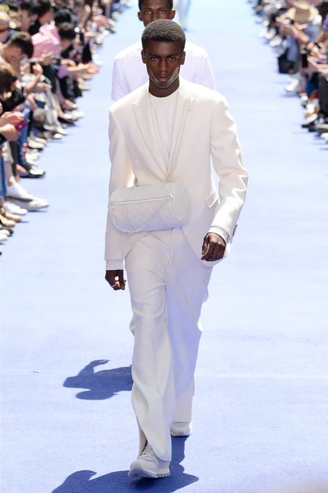 ヴァージル・アブローが手がけた Louis Vuitton 2019年春夏コレクションが遂にお披露目 ファッション界に後世まで語り継がれる歴史的1ページが追加される 〈Louis Vuitton(ルイ ヴィトン)〉がVirgil Abloh(ヴァージル・アブロー)のアーティスティック・ディレクター就任を発表してから早3ヶ月、遂に今をときめくデザイナーの〈LV〉デビューとなる2019年春夏コレクションがお披露目を迎えた。 晴天のパレ・ロワイヤル庭園には、Kanye West(カニエ・ウェスト)とその妻Kim Kardashian(キム・カーダシアン)や、Rihanna(リアーナ)、Kylie Jenner(カイリー・ジェンナー)、A$AP Rocky(エイサップ・ロッキー)、村上隆など、Virgilの友人でもある豪華ゲストが集結。ヒップホップとジャズを繋ぐ成長著しいカルテット、BadBadNotGood(バッドバッドノットグッド)がサウンドトラックを提供したランウェイには、Kid Cudi(キッド・カディ)、Dev Hynes(デヴ・ハインズ)、A$AP Nast(エイサップ・ナスト)、Playboi Carti(プレイボーイ・カルティ)、Theophilus London(テオフィルス・ロンドン)、そして〈Palace(パレス)〉よりLucien Clarke(ルシアン・クラーク)とBlondey McCoy(ブロンディ・マッコイ)らがモデルに起用された。 全56体のルックでは、〈Off-White™️(オフホワイト)〉の党首の真髄である“ラグジュアリーとストリートの融合”が力強さとともに解き放たれた。タイダイ、フローラルパターン、来年80周年を迎える映画『オズの魔法使い』とのコラボレーションなど、必要最小限でありながらも視覚的魅力を放つアイテムがコレクションにエンターテイメント性を付与し、ドラマチックな雰囲気を醸すそのランウェイでは、ルーズフィットのパンツやユーティリティベスト、シアーシャツ、フーディ、仕立ての良いトレンチコートなどがカラーパレットごとに紹介されていく。また、昨日Virgil本人が先行公開したバスケットシューズ風の一足を含め、フットウェアはハイトップシルエットを中心に構成され、上質なドレスシューズもシューレースの配色で遊びをプラス。加えて、〈Louis Vuitton〉の象徴とも言えるラゲージ類は、モノグラムをエンボス加工した半透明の素材やチェーンの斬新な組み合わせにより、良い意味でモードの品格を削ぎ落とした仕上がりにより、観衆の目を釘付けにした。 大喝采の中で迎えたフィナーレではVirgilが涙を流しながら花道を歩き抜け、自身の師匠であるKanyeと熱い抱擁を交わすシーンも。そんな〈Louis Vuitton〉、そしてVirgilの歴史的一幕を是非、上のフォトギャラリーからチェックしてみてはいかがだろうか。