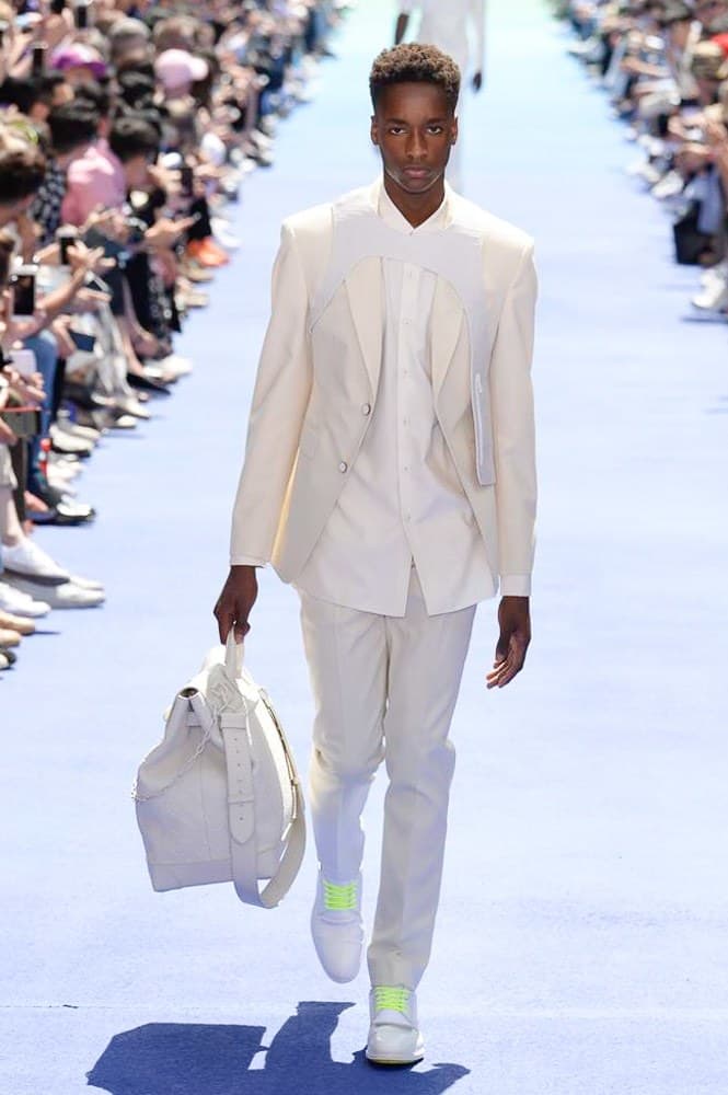 ヴァージル・アブローが手がけた Louis Vuitton 2019年春夏コレクションが遂にお披露目 ファッション界に後世まで語り継がれる歴史的1ページが追加される 〈Louis Vuitton(ルイ ヴィトン)〉がVirgil Abloh(ヴァージル・アブロー)のアーティスティック・ディレクター就任を発表してから早3ヶ月、遂に今をときめくデザイナーの〈LV〉デビューとなる2019年春夏コレクションがお披露目を迎えた。 晴天のパレ・ロワイヤル庭園には、Kanye West(カニエ・ウェスト)とその妻Kim Kardashian(キム・カーダシアン)や、Rihanna(リアーナ)、Kylie Jenner(カイリー・ジェンナー)、A$AP Rocky(エイサップ・ロッキー)、村上隆など、Virgilの友人でもある豪華ゲストが集結。ヒップホップとジャズを繋ぐ成長著しいカルテット、BadBadNotGood(バッドバッドノットグッド)がサウンドトラックを提供したランウェイには、Kid Cudi(キッド・カディ)、Dev Hynes(デヴ・ハインズ)、A$AP Nast(エイサップ・ナスト)、Playboi Carti(プレイボーイ・カルティ)、Theophilus London(テオフィルス・ロンドン)、そして〈Palace(パレス)〉よりLucien Clarke(ルシアン・クラーク)とBlondey McCoy(ブロンディ・マッコイ)らがモデルに起用された。 全56体のルックでは、〈Off-White™️(オフホワイト)〉の党首の真髄である“ラグジュアリーとストリートの融合”が力強さとともに解き放たれた。タイダイ、フローラルパターン、来年80周年を迎える映画『オズの魔法使い』とのコラボレーションなど、必要最小限でありながらも視覚的魅力を放つアイテムがコレクションにエンターテイメント性を付与し、ドラマチックな雰囲気を醸すそのランウェイでは、ルーズフィットのパンツやユーティリティベスト、シアーシャツ、フーディ、仕立ての良いトレンチコートなどがカラーパレットごとに紹介されていく。また、昨日Virgil本人が先行公開したバスケットシューズ風の一足を含め、フットウェアはハイトップシルエットを中心に構成され、上質なドレスシューズもシューレースの配色で遊びをプラス。加えて、〈Louis Vuitton〉の象徴とも言えるラゲージ類は、モノグラムをエンボス加工した半透明の素材やチェーンの斬新な組み合わせにより、良い意味でモードの品格を削ぎ落とした仕上がりにより、観衆の目を釘付けにした。 大喝采の中で迎えたフィナーレではVirgilが涙を流しながら花道を歩き抜け、自身の師匠であるKanyeと熱い抱擁を交わすシーンも。そんな〈Louis Vuitton〉、そしてVirgilの歴史的一幕を是非、上のフォトギャラリーからチェックしてみてはいかがだろうか。