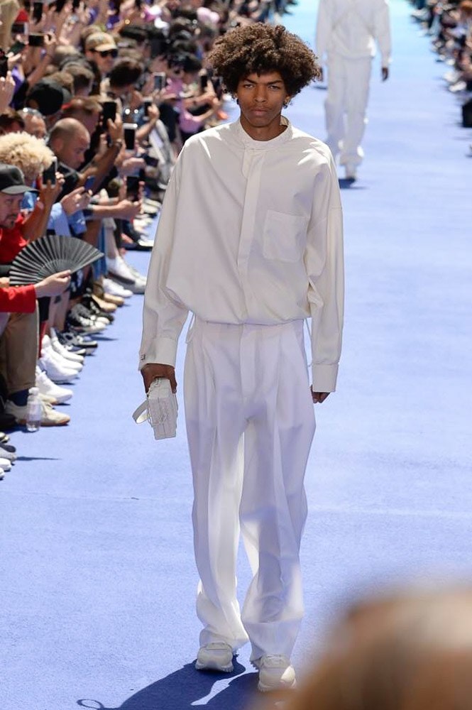 ヴァージル・アブローが手がけた Louis Vuitton 2019年春夏コレクションが遂にお披露目 ファッション界に後世まで語り継がれる歴史的1ページが追加される 〈Louis Vuitton（ルイ ヴィトン）〉がVirgil Abloh（ヴァージル・アブロー）のアーティスティック・ディレクター就任を発表してから早3ヶ月、遂に今をときめくデザイナーの〈LV〉デビューとなる2019年春夏コレクションがお披露目を迎えた。  晴天のパレ・ロワイヤル庭園には、Kanye West（カニエ・ウェスト）とその妻Kim Kardashian（キム・カーダシアン）や、Rihanna（リアーナ）、Kylie Jenner（カイリー・ジェンナー）、A$AP Rocky（エイサップ・ロッキー）、村上隆など、Virgilの友人でもある豪華ゲストが集結。ヒップホップとジャズを繋ぐ成長著しいカルテット、BadBadNotGood（バッドバッドノットグッド）がサウンドトラックを提供したランウェイには、Kid Cudi（キッド・カディ）、Dev Hynes（デヴ・ハインズ）、A$AP Nast（エイサップ・ナスト）、Playboi Carti（プレイボーイ・カルティ）、Theophilus London（テオフィルス・ロンドン）、そして〈Palace（パレス）〉よりLucien Clarke（ルシアン・クラーク）とBlondey McCoy（ブロンディ・マッコイ）らがモデルに起用された。  全56体のルックでは、〈Off-White™️（オフホワイト）〉の党首の真髄である“ラグジュアリーとストリートの融合”が力強さとともに解き放たれた。タイダイ、フローラルパターン、来年80周年を迎える映画『オズの魔法使い』とのコラボレーションなど、必要最小限でありながらも視覚的魅力を放つアイテムがコレクションにエンターテイメント性を付与し、ドラマチックな雰囲気を醸すそのランウェイでは、ルーズフィットのパンツやユーティリティベスト、シアーシャツ、フーディ、仕立ての良いトレンチコートなどがカラーパレットごとに紹介されていく。また、昨日Virgil本人が先行公開したバスケットシューズ風の一足を含め、フットウェアはハイトップシルエットを中心に構成され、上質なドレスシューズもシューレースの配色で遊びをプラス。加えて、〈Louis Vuitton〉の象徴とも言えるラゲージ類は、モノグラムをエンボス加工した半透明の素材やチェーンの斬新な組み合わせにより、良い意味でモードの品格を削ぎ落とした仕上がりにより、観衆の目を釘付けにした。  大喝采の中で迎えたフィナーレではVirgilが涙を流しながら花道を歩き抜け、自身の師匠であるKanyeと熱い抱擁を交わすシーンも。そんな〈Louis Vuitton〉、そしてVirgilの歴史的一幕を是非、上のフォトギャラリーからチェックしてみてはいかがだろうか。