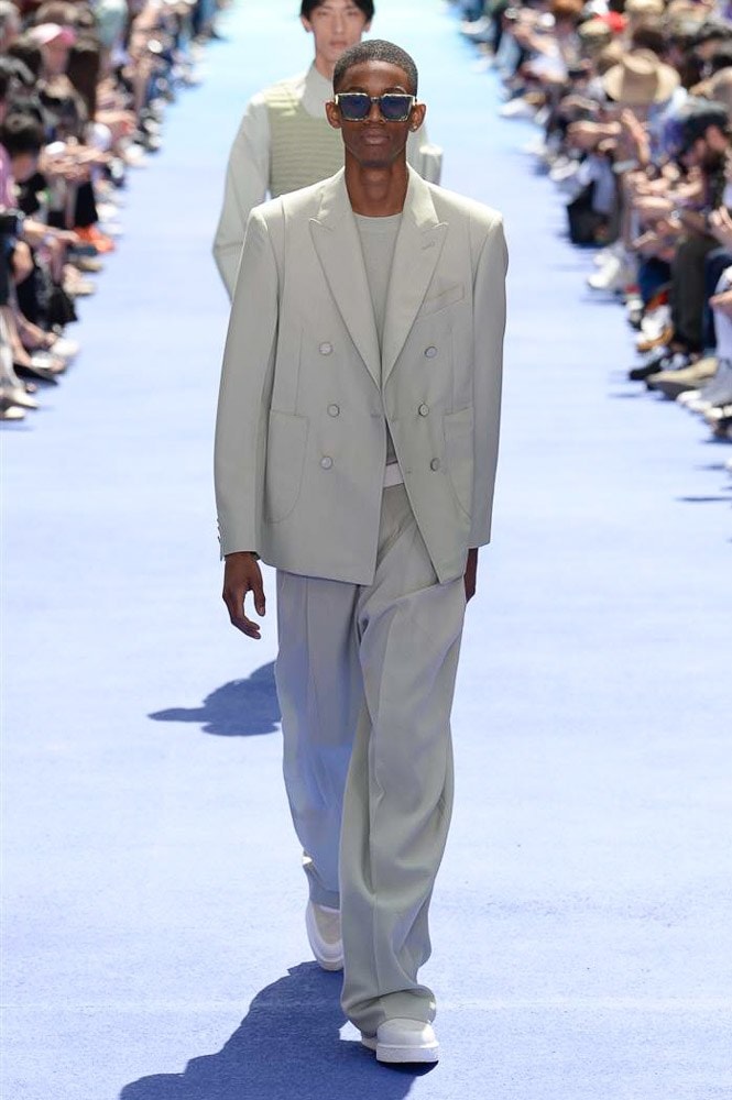 ヴァージル・アブローが手がけた Louis Vuitton 2019年春夏コレクションが遂にお披露目 ファッション界に後世まで語り継がれる歴史的1ページが追加される 〈Louis Vuitton（ルイ ヴィトン）〉がVirgil Abloh（ヴァージル・アブロー）のアーティスティック・ディレクター就任を発表してから早3ヶ月、遂に今をときめくデザイナーの〈LV〉デビューとなる2019年春夏コレクションがお披露目を迎えた。  晴天のパレ・ロワイヤル庭園には、Kanye West（カニエ・ウェスト）とその妻Kim Kardashian（キム・カーダシアン）や、Rihanna（リアーナ）、Kylie Jenner（カイリー・ジェンナー）、A$AP Rocky（エイサップ・ロッキー）、村上隆など、Virgilの友人でもある豪華ゲストが集結。ヒップホップとジャズを繋ぐ成長著しいカルテット、BadBadNotGood（バッドバッドノットグッド）がサウンドトラックを提供したランウェイには、Kid Cudi（キッド・カディ）、Dev Hynes（デヴ・ハインズ）、A$AP Nast（エイサップ・ナスト）、Playboi Carti（プレイボーイ・カルティ）、Theophilus London（テオフィルス・ロンドン）、そして〈Palace（パレス）〉よりLucien Clarke（ルシアン・クラーク）とBlondey McCoy（ブロンディ・マッコイ）らがモデルに起用された。  全56体のルックでは、〈Off-White™️（オフホワイト）〉の党首の真髄である“ラグジュアリーとストリートの融合”が力強さとともに解き放たれた。タイダイ、フローラルパターン、来年80周年を迎える映画『オズの魔法使い』とのコラボレーションなど、必要最小限でありながらも視覚的魅力を放つアイテムがコレクションにエンターテイメント性を付与し、ドラマチックな雰囲気を醸すそのランウェイでは、ルーズフィットのパンツやユーティリティベスト、シアーシャツ、フーディ、仕立ての良いトレンチコートなどがカラーパレットごとに紹介されていく。また、昨日Virgil本人が先行公開したバスケットシューズ風の一足を含め、フットウェアはハイトップシルエットを中心に構成され、上質なドレスシューズもシューレースの配色で遊びをプラス。加えて、〈Louis Vuitton〉の象徴とも言えるラゲージ類は、モノグラムをエンボス加工した半透明の素材やチェーンの斬新な組み合わせにより、良い意味でモードの品格を削ぎ落とした仕上がりにより、観衆の目を釘付けにした。  大喝采の中で迎えたフィナーレではVirgilが涙を流しながら花道を歩き抜け、自身の師匠であるKanyeと熱い抱擁を交わすシーンも。そんな〈Louis Vuitton〉、そしてVirgilの歴史的一幕を是非、上のフォトギャラリーからチェックしてみてはいかがだろうか。