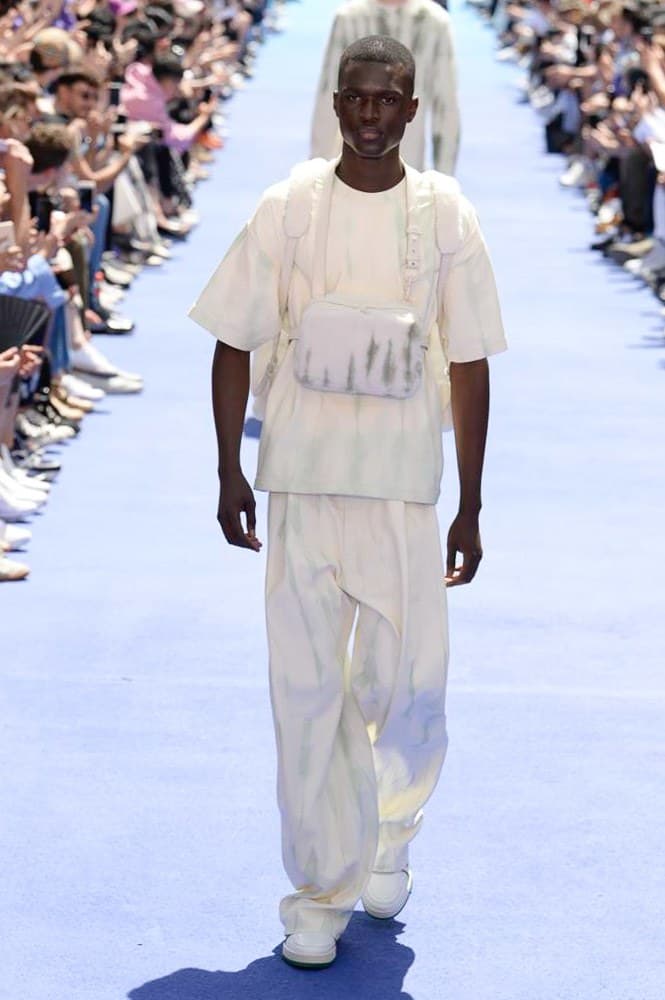 ヴァージル・アブローが手がけた Louis Vuitton 2019年春夏コレクションが遂にお披露目 ファッション界に後世まで語り継がれる歴史的1ページが追加される 〈Louis Vuitton(ルイ ヴィトン)〉がVirgil Abloh(ヴァージル・アブロー)のアーティスティック・ディレクター就任を発表してから早3ヶ月、遂に今をときめくデザイナーの〈LV〉デビューとなる2019年春夏コレクションがお披露目を迎えた。 晴天のパレ・ロワイヤル庭園には、Kanye West(カニエ・ウェスト)とその妻Kim Kardashian(キム・カーダシアン)や、Rihanna(リアーナ)、Kylie Jenner(カイリー・ジェンナー)、A$AP Rocky(エイサップ・ロッキー)、村上隆など、Virgilの友人でもある豪華ゲストが集結。ヒップホップとジャズを繋ぐ成長著しいカルテット、BadBadNotGood(バッドバッドノットグッド)がサウンドトラックを提供したランウェイには、Kid Cudi(キッド・カディ)、Dev Hynes(デヴ・ハインズ)、A$AP Nast(エイサップ・ナスト)、Playboi Carti(プレイボーイ・カルティ)、Theophilus London(テオフィルス・ロンドン)、そして〈Palace(パレス)〉よりLucien Clarke(ルシアン・クラーク)とBlondey McCoy(ブロンディ・マッコイ)らがモデルに起用された。 全56体のルックでは、〈Off-White™️(オフホワイト)〉の党首の真髄である“ラグジュアリーとストリートの融合”が力強さとともに解き放たれた。タイダイ、フローラルパターン、来年80周年を迎える映画『オズの魔法使い』とのコラボレーションなど、必要最小限でありながらも視覚的魅力を放つアイテムがコレクションにエンターテイメント性を付与し、ドラマチックな雰囲気を醸すそのランウェイでは、ルーズフィットのパンツやユーティリティベスト、シアーシャツ、フーディ、仕立ての良いトレンチコートなどがカラーパレットごとに紹介されていく。また、昨日Virgil本人が先行公開したバスケットシューズ風の一足を含め、フットウェアはハイトップシルエットを中心に構成され、上質なドレスシューズもシューレースの配色で遊びをプラス。加えて、〈Louis Vuitton〉の象徴とも言えるラゲージ類は、モノグラムをエンボス加工した半透明の素材やチェーンの斬新な組み合わせにより、良い意味でモードの品格を削ぎ落とした仕上がりにより、観衆の目を釘付けにした。 大喝采の中で迎えたフィナーレではVirgilが涙を流しながら花道を歩き抜け、自身の師匠であるKanyeと熱い抱擁を交わすシーンも。そんな〈Louis Vuitton〉、そしてVirgilの歴史的一幕を是非、上のフォトギャラリーからチェックしてみてはいかがだろうか。