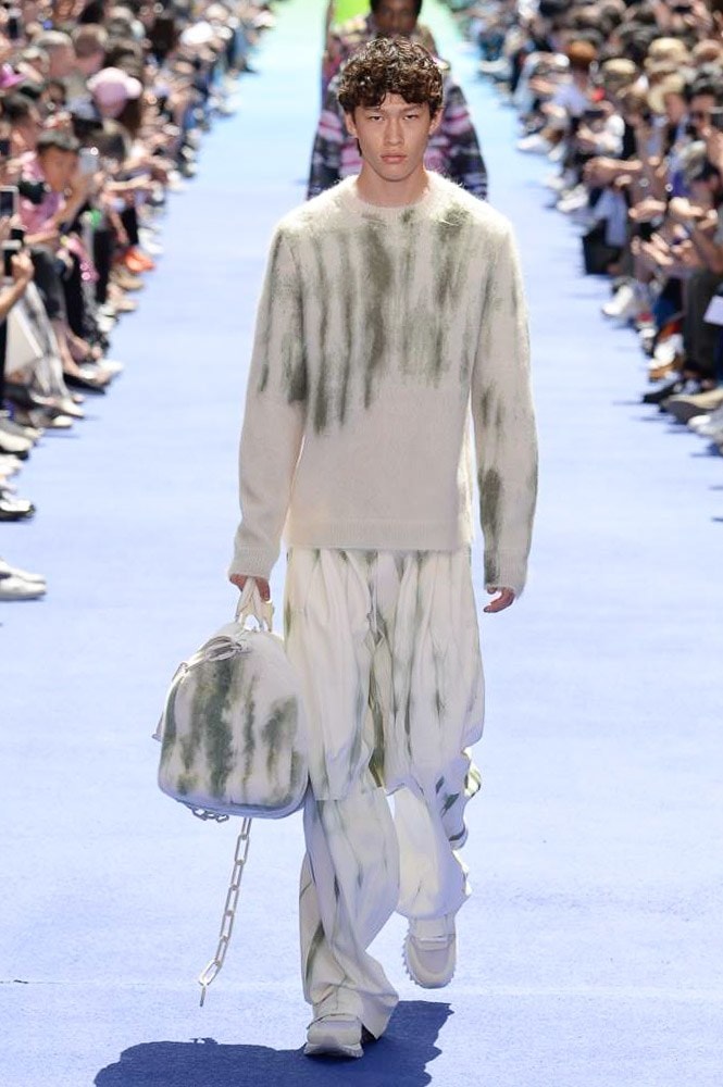 ヴァージル・アブローが手がけた Louis Vuitton 2019年春夏コレクションが遂にお披露目 ファッション界に後世まで語り継がれる歴史的1ページが追加される 〈Louis Vuitton（ルイ ヴィトン）〉がVirgil Abloh（ヴァージル・アブロー）のアーティスティック・ディレクター就任を発表してから早3ヶ月、遂に今をときめくデザイナーの〈LV〉デビューとなる2019年春夏コレクションがお披露目を迎えた。  晴天のパレ・ロワイヤル庭園には、Kanye West（カニエ・ウェスト）とその妻Kim Kardashian（キム・カーダシアン）や、Rihanna（リアーナ）、Kylie Jenner（カイリー・ジェンナー）、A$AP Rocky（エイサップ・ロッキー）、村上隆など、Virgilの友人でもある豪華ゲストが集結。ヒップホップとジャズを繋ぐ成長著しいカルテット、BadBadNotGood（バッドバッドノットグッド）がサウンドトラックを提供したランウェイには、Kid Cudi（キッド・カディ）、Dev Hynes（デヴ・ハインズ）、A$AP Nast（エイサップ・ナスト）、Playboi Carti（プレイボーイ・カルティ）、Theophilus London（テオフィルス・ロンドン）、そして〈Palace（パレス）〉よりLucien Clarke（ルシアン・クラーク）とBlondey McCoy（ブロンディ・マッコイ）らがモデルに起用された。  全56体のルックでは、〈Off-White™️（オフホワイト）〉の党首の真髄である“ラグジュアリーとストリートの融合”が力強さとともに解き放たれた。タイダイ、フローラルパターン、来年80周年を迎える映画『オズの魔法使い』とのコラボレーションなど、必要最小限でありながらも視覚的魅力を放つアイテムがコレクションにエンターテイメント性を付与し、ドラマチックな雰囲気を醸すそのランウェイでは、ルーズフィットのパンツやユーティリティベスト、シアーシャツ、フーディ、仕立ての良いトレンチコートなどがカラーパレットごとに紹介されていく。また、昨日Virgil本人が先行公開したバスケットシューズ風の一足を含め、フットウェアはハイトップシルエットを中心に構成され、上質なドレスシューズもシューレースの配色で遊びをプラス。加えて、〈Louis Vuitton〉の象徴とも言えるラゲージ類は、モノグラムをエンボス加工した半透明の素材やチェーンの斬新な組み合わせにより、良い意味でモードの品格を削ぎ落とした仕上がりにより、観衆の目を釘付けにした。  大喝采の中で迎えたフィナーレではVirgilが涙を流しながら花道を歩き抜け、自身の師匠であるKanyeと熱い抱擁を交わすシーンも。そんな〈Louis Vuitton〉、そしてVirgilの歴史的一幕を是非、上のフォトギャラリーからチェックしてみてはいかがだろうか。