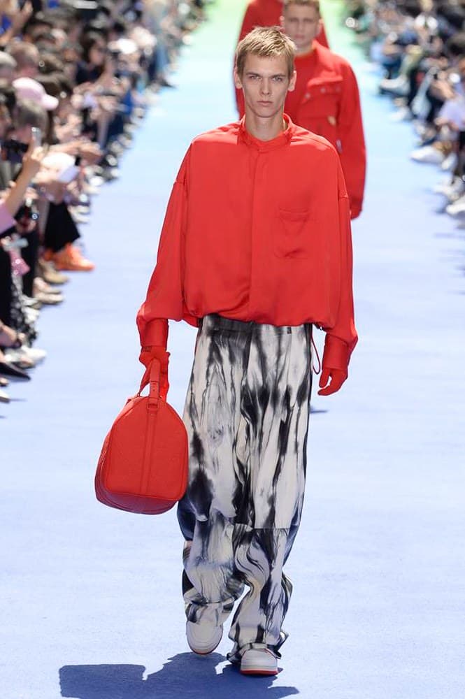 ヴァージル・アブローが手がけた Louis Vuitton 2019年春夏コレクションが遂にお披露目 ファッション界に後世まで語り継がれる歴史的1ページが追加される 〈Louis Vuitton(ルイ ヴィトン)〉がVirgil Abloh(ヴァージル・アブロー)のアーティスティック・ディレクター就任を発表してから早3ヶ月、遂に今をときめくデザイナーの〈LV〉デビューとなる2019年春夏コレクションがお披露目を迎えた。 晴天のパレ・ロワイヤル庭園には、Kanye West(カニエ・ウェスト)とその妻Kim Kardashian(キム・カーダシアン)や、Rihanna(リアーナ)、Kylie Jenner(カイリー・ジェンナー)、A$AP Rocky(エイサップ・ロッキー)、村上隆など、Virgilの友人でもある豪華ゲストが集結。ヒップホップとジャズを繋ぐ成長著しいカルテット、BadBadNotGood(バッドバッドノットグッド)がサウンドトラックを提供したランウェイには、Kid Cudi(キッド・カディ)、Dev Hynes(デヴ・ハインズ)、A$AP Nast(エイサップ・ナスト)、Playboi Carti(プレイボーイ・カルティ)、Theophilus London(テオフィルス・ロンドン)、そして〈Palace(パレス)〉よりLucien Clarke(ルシアン・クラーク)とBlondey McCoy(ブロンディ・マッコイ)らがモデルに起用された。 全56体のルックでは、〈Off-White™️(オフホワイト)〉の党首の真髄である“ラグジュアリーとストリートの融合”が力強さとともに解き放たれた。タイダイ、フローラルパターン、来年80周年を迎える映画『オズの魔法使い』とのコラボレーションなど、必要最小限でありながらも視覚的魅力を放つアイテムがコレクションにエンターテイメント性を付与し、ドラマチックな雰囲気を醸すそのランウェイでは、ルーズフィットのパンツやユーティリティベスト、シアーシャツ、フーディ、仕立ての良いトレンチコートなどがカラーパレットごとに紹介されていく。また、昨日Virgil本人が先行公開したバスケットシューズ風の一足を含め、フットウェアはハイトップシルエットを中心に構成され、上質なドレスシューズもシューレースの配色で遊びをプラス。加えて、〈Louis Vuitton〉の象徴とも言えるラゲージ類は、モノグラムをエンボス加工した半透明の素材やチェーンの斬新な組み合わせにより、良い意味でモードの品格を削ぎ落とした仕上がりにより、観衆の目を釘付けにした。 大喝采の中で迎えたフィナーレではVirgilが涙を流しながら花道を歩き抜け、自身の師匠であるKanyeと熱い抱擁を交わすシーンも。そんな〈Louis Vuitton〉、そしてVirgilの歴史的一幕を是非、上のフォトギャラリーからチェックしてみてはいかがだろうか。