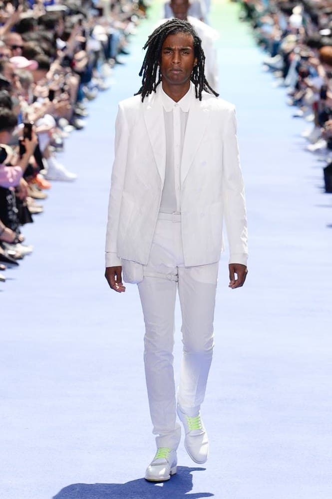 ヴァージル・アブローが手がけた Louis Vuitton 2019年春夏コレクションが遂にお披露目 ファッション界に後世まで語り継がれる歴史的1ページが追加される 〈Louis Vuitton(ルイ ヴィトン)〉がVirgil Abloh(ヴァージル・アブロー)のアーティスティック・ディレクター就任を発表してから早3ヶ月、遂に今をときめくデザイナーの〈LV〉デビューとなる2019年春夏コレクションがお披露目を迎えた。 晴天のパレ・ロワイヤル庭園には、Kanye West(カニエ・ウェスト)とその妻Kim Kardashian(キム・カーダシアン)や、Rihanna(リアーナ)、Kylie Jenner(カイリー・ジェンナー)、A$AP Rocky(エイサップ・ロッキー)、村上隆など、Virgilの友人でもある豪華ゲストが集結。ヒップホップとジャズを繋ぐ成長著しいカルテット、BadBadNotGood(バッドバッドノットグッド)がサウンドトラックを提供したランウェイには、Kid Cudi(キッド・カディ)、Dev Hynes(デヴ・ハインズ)、A$AP Nast(エイサップ・ナスト)、Playboi Carti(プレイボーイ・カルティ)、Theophilus London(テオフィルス・ロンドン)、そして〈Palace(パレス)〉よりLucien Clarke(ルシアン・クラーク)とBlondey McCoy(ブロンディ・マッコイ)らがモデルに起用された。 全56体のルックでは、〈Off-White™️(オフホワイト)〉の党首の真髄である“ラグジュアリーとストリートの融合”が力強さとともに解き放たれた。タイダイ、フローラルパターン、来年80周年を迎える映画『オズの魔法使い』とのコラボレーションなど、必要最小限でありながらも視覚的魅力を放つアイテムがコレクションにエンターテイメント性を付与し、ドラマチックな雰囲気を醸すそのランウェイでは、ルーズフィットのパンツやユーティリティベスト、シアーシャツ、フーディ、仕立ての良いトレンチコートなどがカラーパレットごとに紹介されていく。また、昨日Virgil本人が先行公開したバスケットシューズ風の一足を含め、フットウェアはハイトップシルエットを中心に構成され、上質なドレスシューズもシューレースの配色で遊びをプラス。加えて、〈Louis Vuitton〉の象徴とも言えるラゲージ類は、モノグラムをエンボス加工した半透明の素材やチェーンの斬新な組み合わせにより、良い意味でモードの品格を削ぎ落とした仕上がりにより、観衆の目を釘付けにした。 大喝采の中で迎えたフィナーレではVirgilが涙を流しながら花道を歩き抜け、自身の師匠であるKanyeと熱い抱擁を交わすシーンも。そんな〈Louis Vuitton〉、そしてVirgilの歴史的一幕を是非、上のフォトギャラリーからチェックしてみてはいかがだろうか。