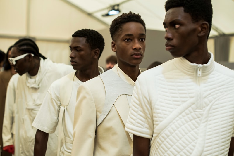 ヴァージル・アブローのビジョンを体現した Louis Vuitton 2019年春夏コレクションのバックステージに潜入 ランウェイルックからは確認することのできない各種アパレル&アクセサリーのディテールを撮影することに成功した服好き必見のフォトセット Virgil Abloh(ヴァージル・アブロー)は、〈Louis Vuitton(ルイ ヴィトン)〉のアーティスティックデザイナー就任後初のランウェイをパリのパレ・ロワイヤル庭園で披露した。歴史的一幕で、今をときめくイリノイ州出身のデザイナーは〈LV〉に未だかつて見たことのない景色を見せたと言っても過言ではないだろう。だが、そのクリエイションの真髄は、バックステージでこそ痛感するものだった。 ベストやポロシャツなどに見られる3Dのジオメトリックパターンで立体感を演出したレイヤード、モノグラムの花型のカフスボタン、大胆な原色使いなど、Virgilは〈Louis Vuitton〉のDNAを従来とは異なるアプローチで体現。また、セーター、スーツ、フーディといったメンズウェアも前衛的なカッティングとステッチワークで新鮮味が付与されると同時に、組み込み式のポーチやジッパー、プルタブなどを応用することで、壮麗なデザインの中にカジュアル/アウトドアウェアに着想を得た機能性を追加している。その一方で、ハイカットシルエットを中心に構成されたスニーカーは、Air Jordanや〈Ewing Athletics(ユーイング アスレチックス)〉などのバスケットシューズを原型に、今後の展開に自然と期待が膨らむデザインのものが数多く出揃った印象だ。そして、言及せずには終われないアクセサリーコレクションだが、ラゲージについてはまさに“型破り”という言葉がよく似合う。Kim Jones(キム・ジョーンズ)政権の頃から変革が見え隠れしたが、建築デザインを背景に持つVirgilが加わったことで、クラシカルなシルエットは全く別物のような表情へと生まれ変わっている。 ランウェイルックからは確認することのできない各プロダクトのディテールワークを是非、上のフォトギャラリーからチェックしてみてほしい。あわせて、本ランウェイのハイライトとも言えるVirgilとKanye West(カニエ・ウェスト)が涙ながらに抱擁しあう感動の1シーンもお見逃しなく。