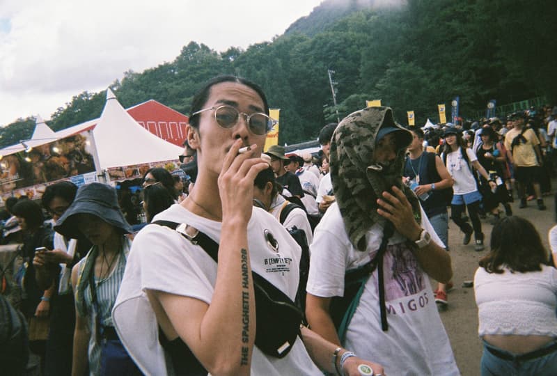 Back to Film:HYPEBEAST 編集部の等身大 FUJI ROCK FESTIVAL '18 備忘録 ファッション業界の方々から学生時代の部活の先輩まで、『HYPEBEAST』のリアルな日常を使い捨てカメラで記録した「FUJI ROCK」の番外編企画 山の天気は変わりやすい。「FUJI ROCK FESTIVAL '18」の会場となった苗場スキー場は途中に台風の通過もあってか、激しい雨と燦々と降り注ぐ日照りの繰り返しで、どこかの先人が作った言葉の意味を再認識した3日間だった。『HYPEBEAST』では連日、臨場感溢れるアーティストのステージパフォーマンスを中心とした速報や、タフな環境下でもファッション>機能性のマインドを持ち合わせる人々を撮影したストリートスナップをご紹介してきた。これらの記事制作の背景に少しだけ触れると、取材は日中から場合によっては深夜にまで及び、翌日朝は写真の編集と記事の執筆、現場では聴きたいアーティストのライブを余裕綽々で堪能できる時間はほとんどなく、山道の移動と悪天候がプレゼントしてくれる疲労の蓄積で、夜はホテルに戻るや否や汗を流し、次の日に備えて寝る、これがリアルである。 しかし、移動の最中や束の間の休憩中に遭遇する、日頃からお世話になっているファッション/音楽業界の方々、夜遊び仲間、中学時代の部活の先輩、久しぶりに会った音好きの友人たちと言い合うライブの感想、たわいもない会話、そしてビールでの乾杯は、編集部にとっては紛れもない「FUJI ROCK」の醍醐味なのだ。 そこで、我々は本気の仕事の裏側で、ポケットに使い捨てカメラを忍ばせ、柵前の景色から美味しいご飯を提供してくれたお食事処の皆さんまで、実際にいたロケーションと遭遇した仕事仲間&友人を気の向くままにパシャパシャと撮影。このカジュアルな企画では、上原のセレクトショップ『UFO(UPPER FIELD ONE)』の千寿公久、過去に#Essentialsに登場してくれた『Mastered』編集長の三木系大、水原佑果や武居詩織&きなりのモデル勢など、レポート記事とストリートスナップには登場していない人の姿も収めることができた。暗かったり、写真の構図が雑だったり、ピントが合っていないのはご愛嬌。是非、『HYPEBEAST』編集部2名が緩めに切り取った「FUJI ROCK FESTIVAL '18」の等身大備忘録を上のフォトギャラリーから楽しんでみてほしい。 まだ「FUJI ROCK FESTIVAL '18」の初日、二日目、最終日のレポートとストリートスナップをチェックしていない方は、そちらもお見逃しなく。