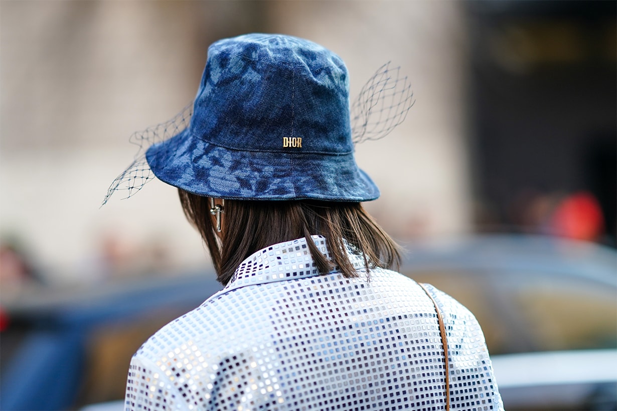 A guest wears a blue tie-and-dye Dior bob hat with a veil, earrings, a glittering mirrored shirt, outside Bottega Veneta, during Milan Fashion Week Fall/Winter 2020-2021 on February 22, 2020 in Milan, Italy.