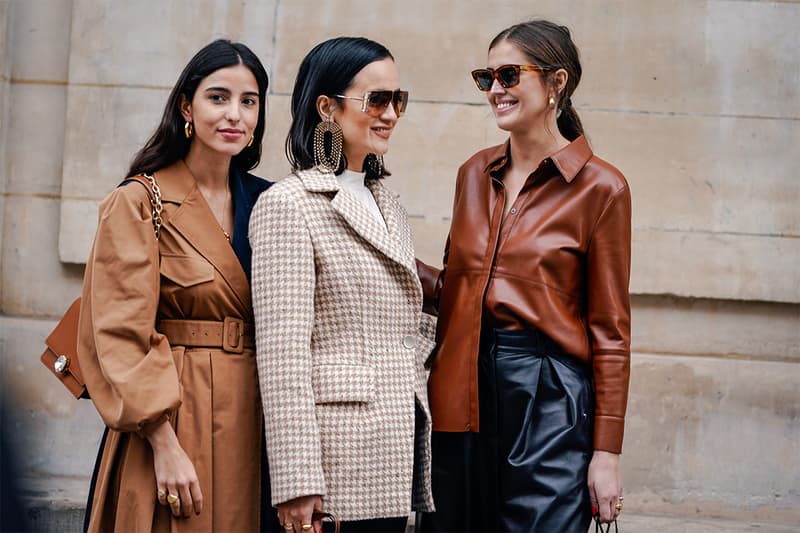 A guest (L) wears earrings, a camel coat, a Miu Miu brown leather bag ; a guest (M) wears sunglasses, earrings, a white hi-neck top, a beige houndstooth jacket ; a guest (R) wears sunglasses, earrings, a brown leather jacket, black leather pants , outside Paul & Joe, during Paris Fashion Week Womenswear Fall/Winter 2019/2020