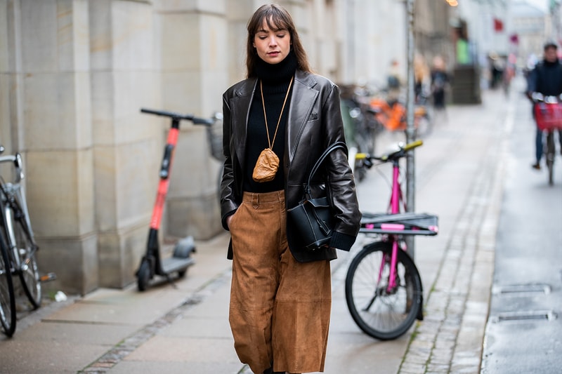 A guest is seen wearing brown velvet cropped pants, black leather jacket, bag around her neck, black bag outside Gestuz on Day 1 during Copenhagen Fashion Week Autumn/Winter 2020 on January 28, 2020 in Copenhagen, Denmark.