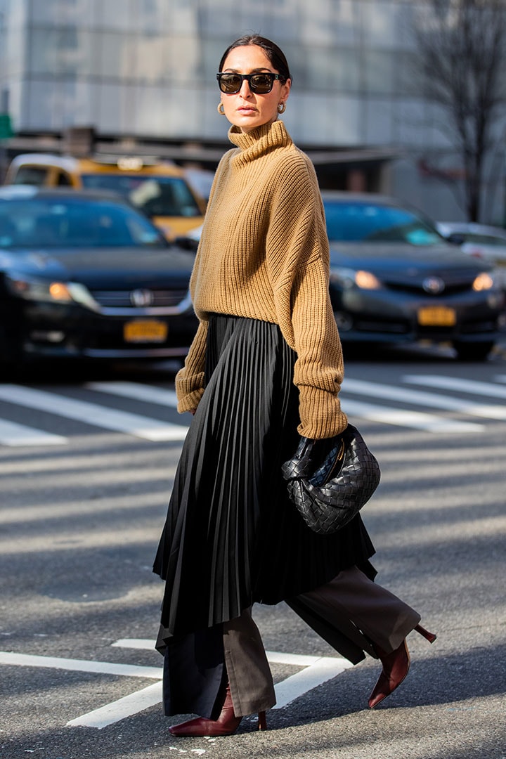 Geraldine Boublil is seen wearing brown turtleneck knit, black asymmetric pleated skirt worn over pants, black Bottega bag outside Tory Burch during New York Fashion Week Fall / Winter on February 09, 2020 in New York City